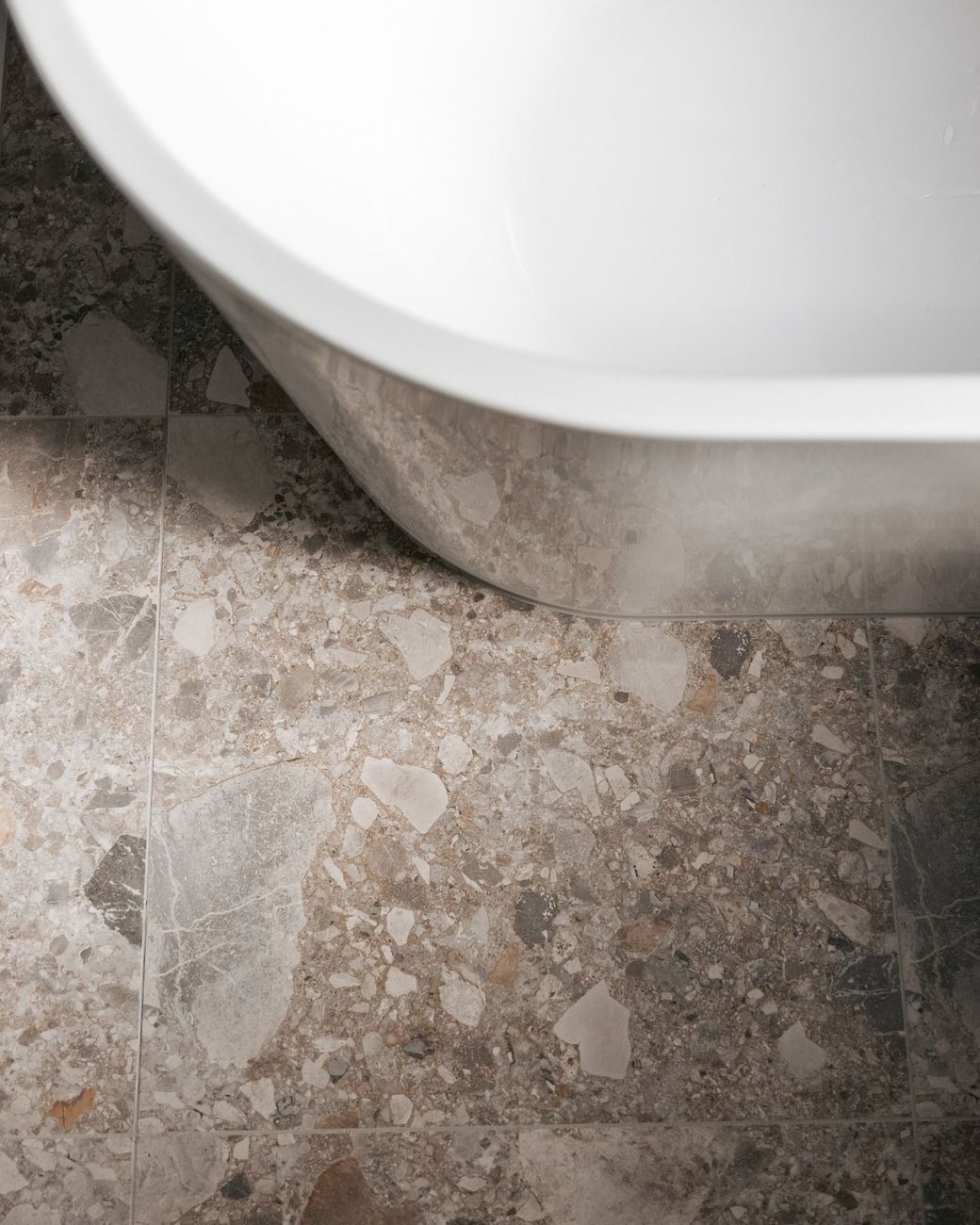 White bathtub edge over a speckled stone floor, close-up of the bathroom corner.