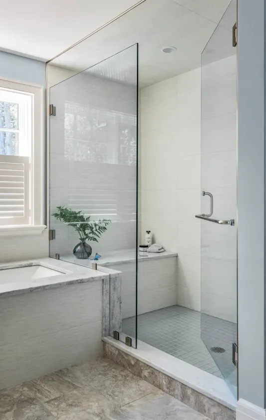 Modern bathroom with glass shower enclosure, gray tile, and a window above a tub wall.
