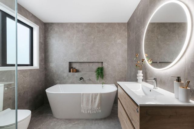 Modern bathroom with freestanding tub, walk-in shower, and illuminated oval mirror.