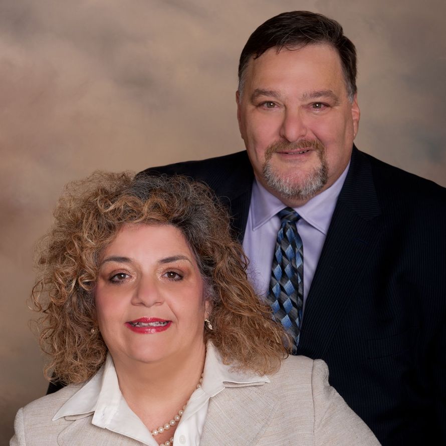 Two smiling adults posed in formal attire against a beige studio backdrop