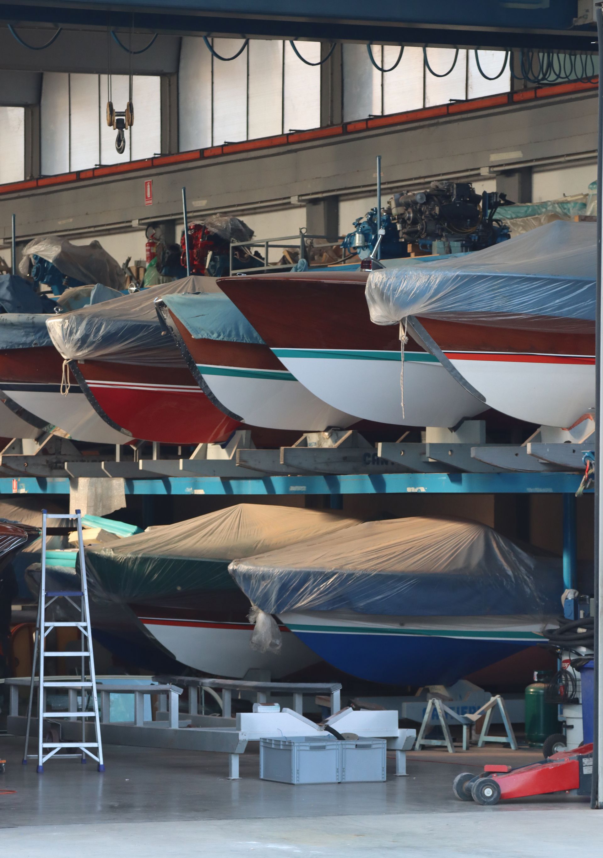 Boats stored in a boathouse, covered in tarps with ladders and tools nearby