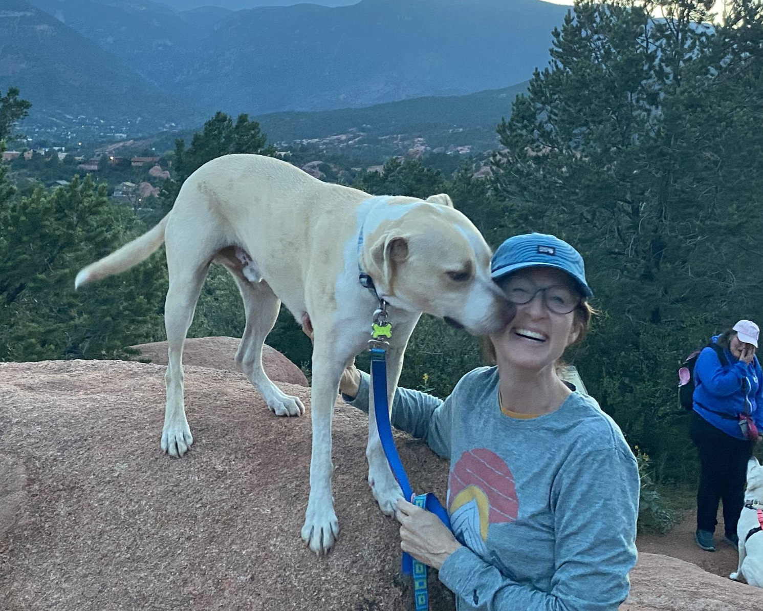 Happy hiker getting dog-on-a-rock kisses from her rescue dogs in front of Pikes Peak