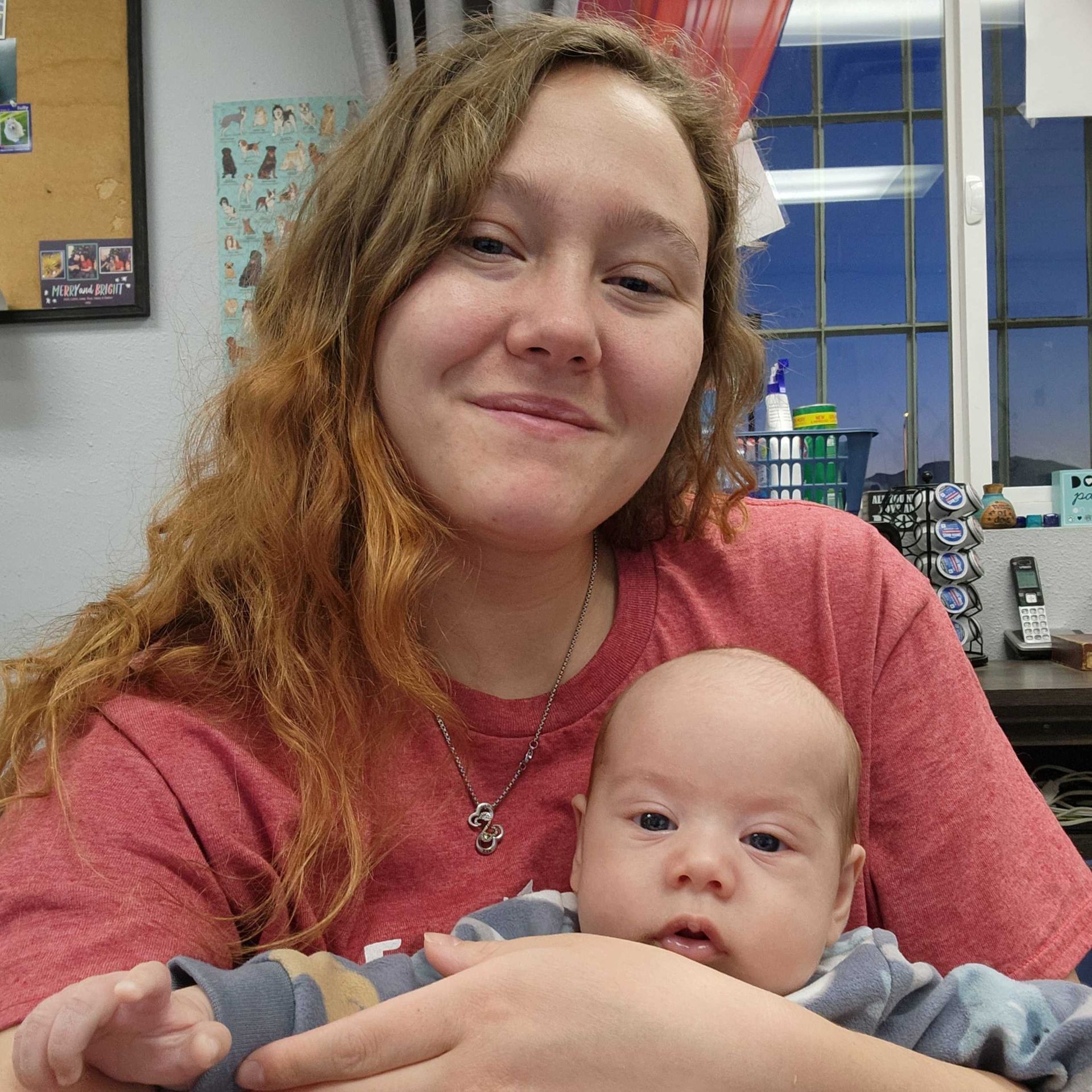 Smiling young woman sitting in an office holding her new son