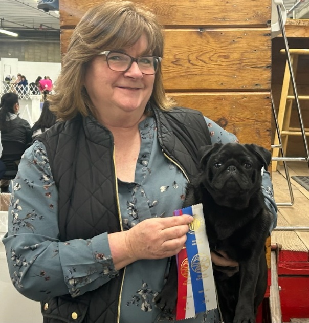 A gleeful woman holds her champion pug who just won Best of Breed!