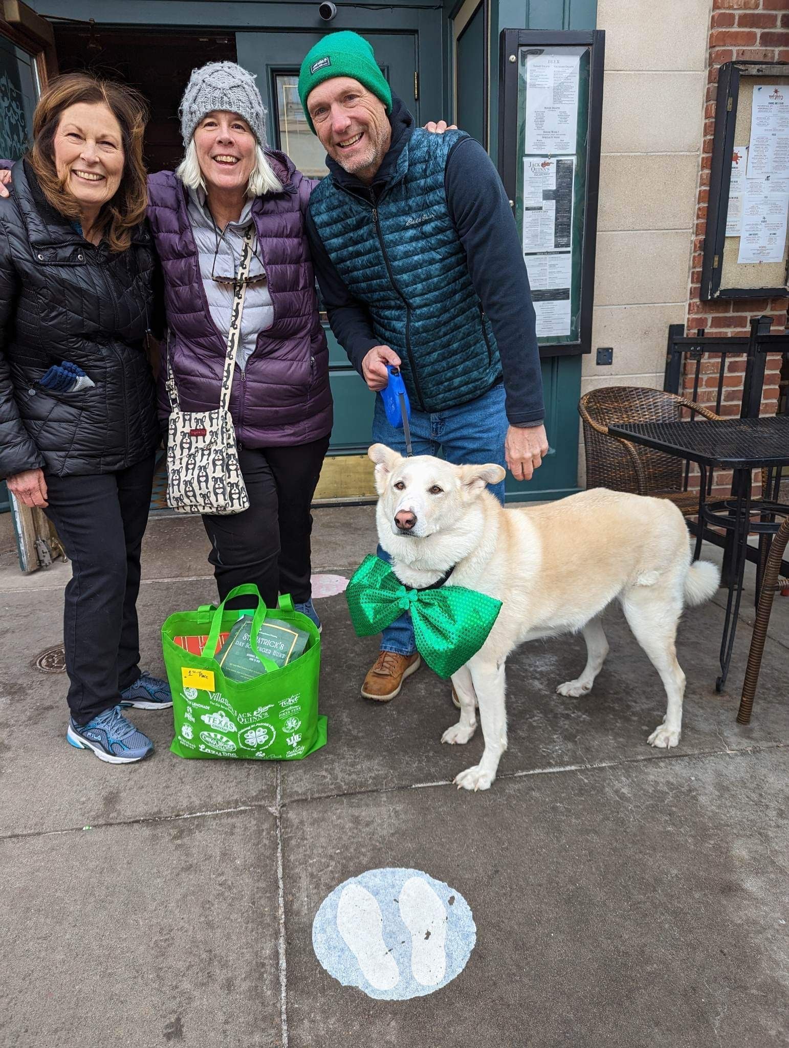 Three people posing with their rescue dog in front of a pub.