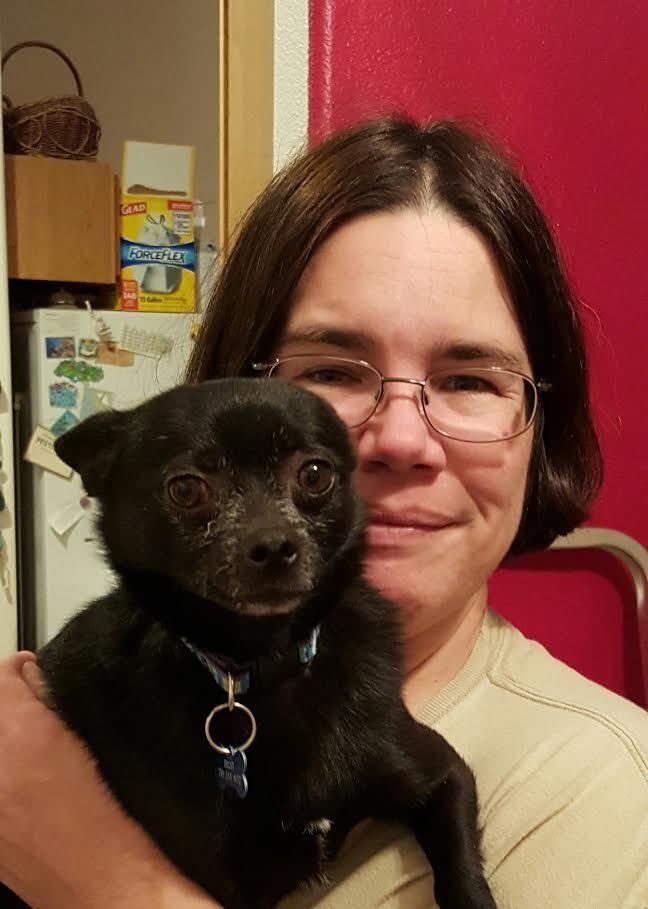 Smiling woman sitting with a small black rescue schipperke mix