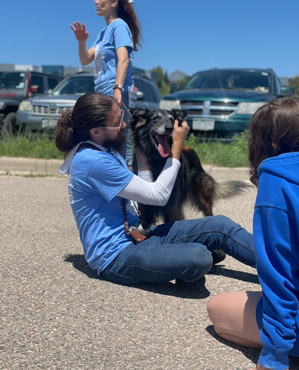 Long haired fellow pets a Belgian Tervuren while sitting on the ground