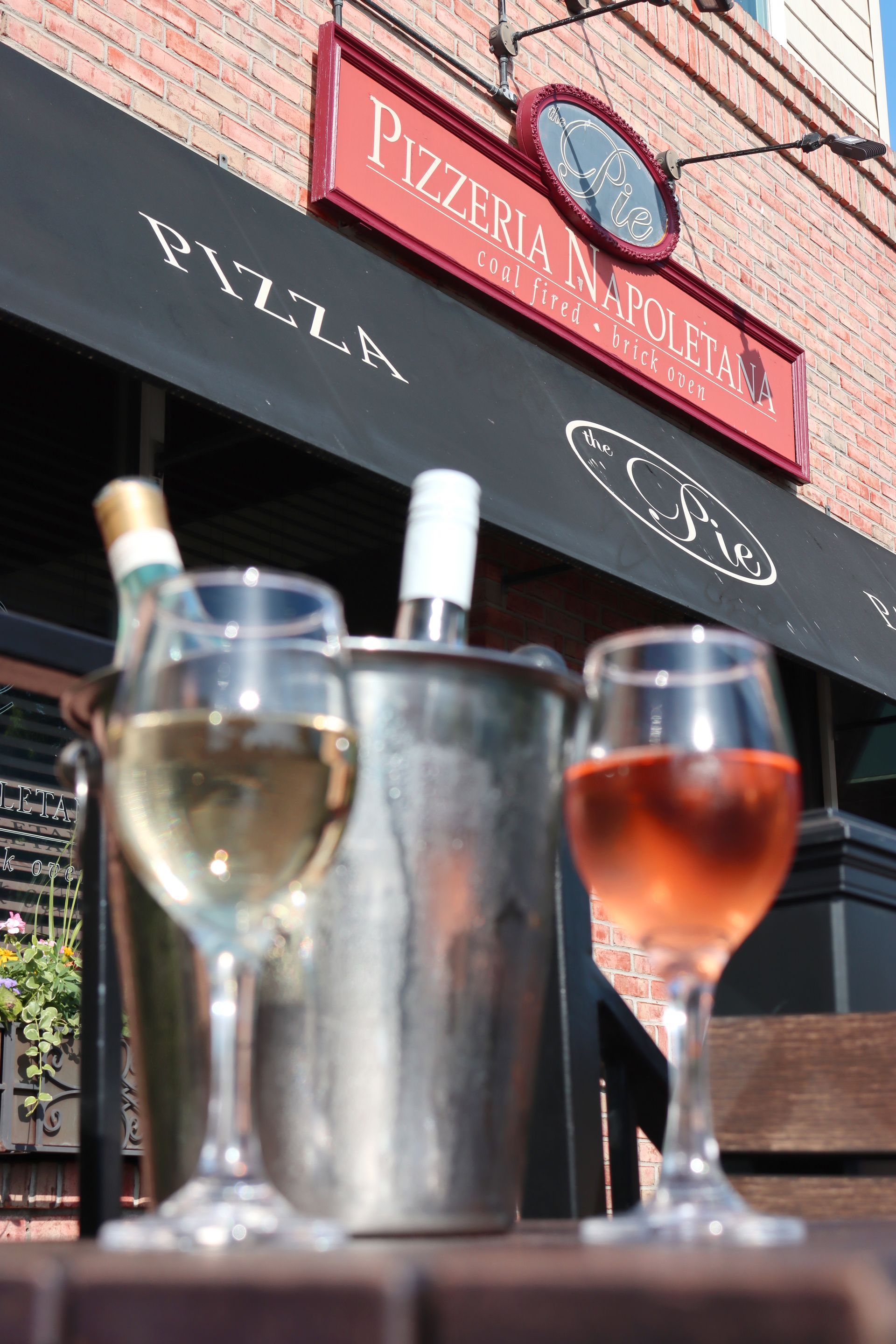 Two glasses of wine are on a table in front of a pizzeria