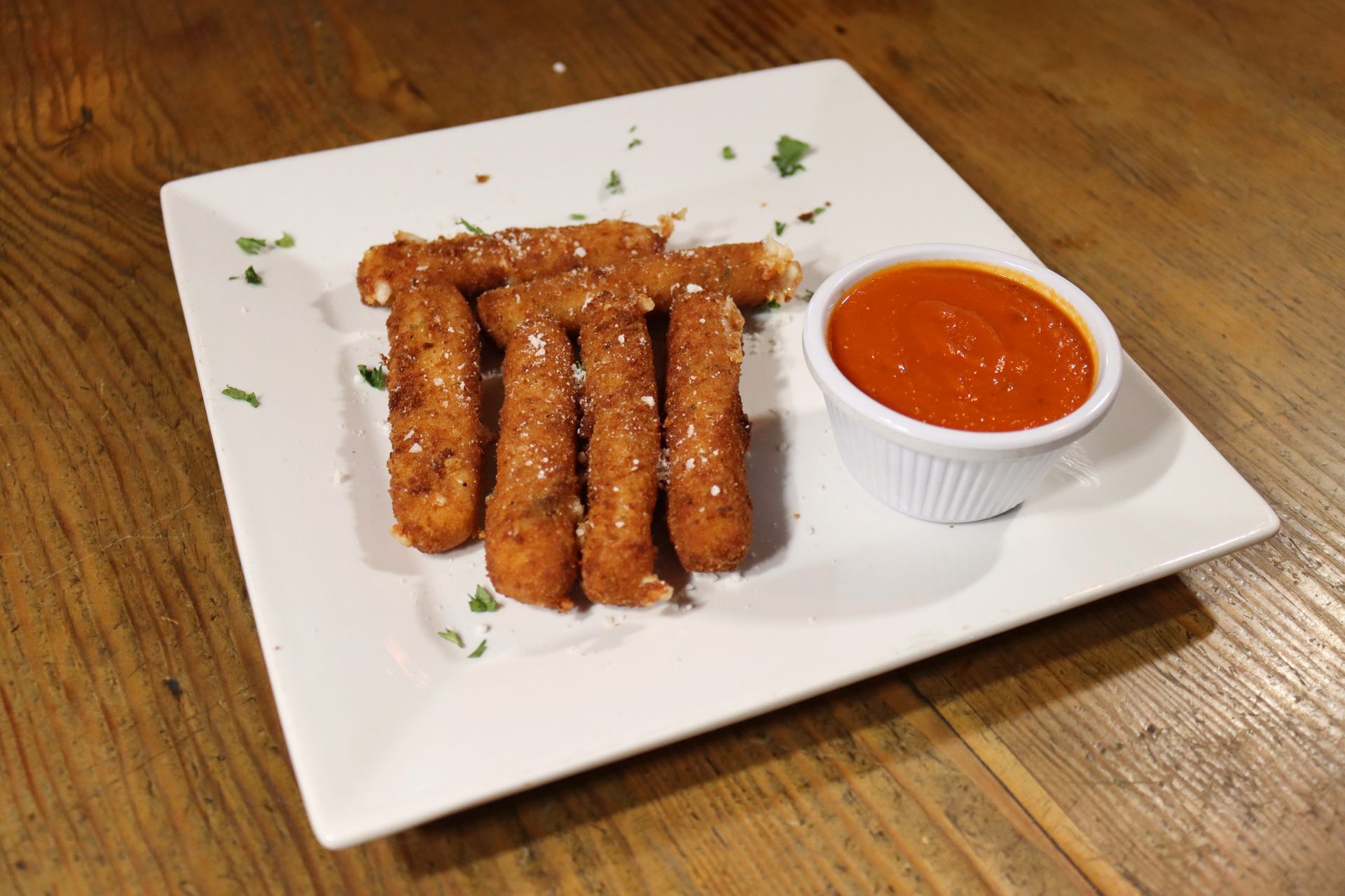 A white plate topped with mozzarella sticks and dipping sauce on a wooden table.