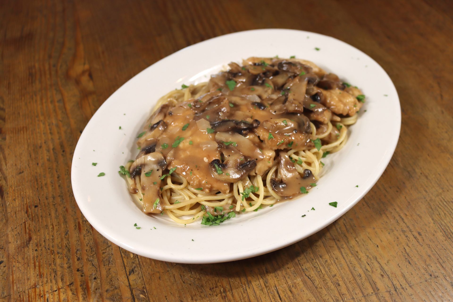 A white plate topped with spaghetti and mushrooms on a wooden table.