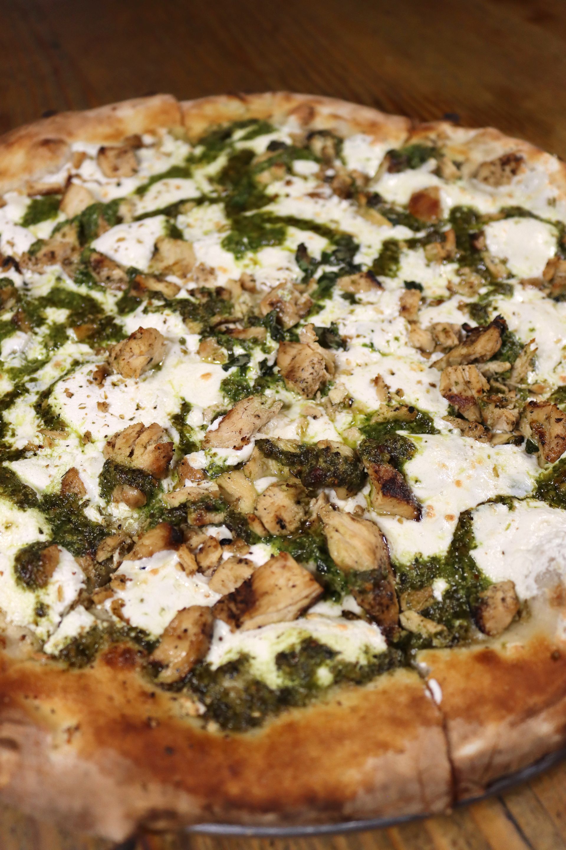 A pizza with chicken and pesto on a wooden table.