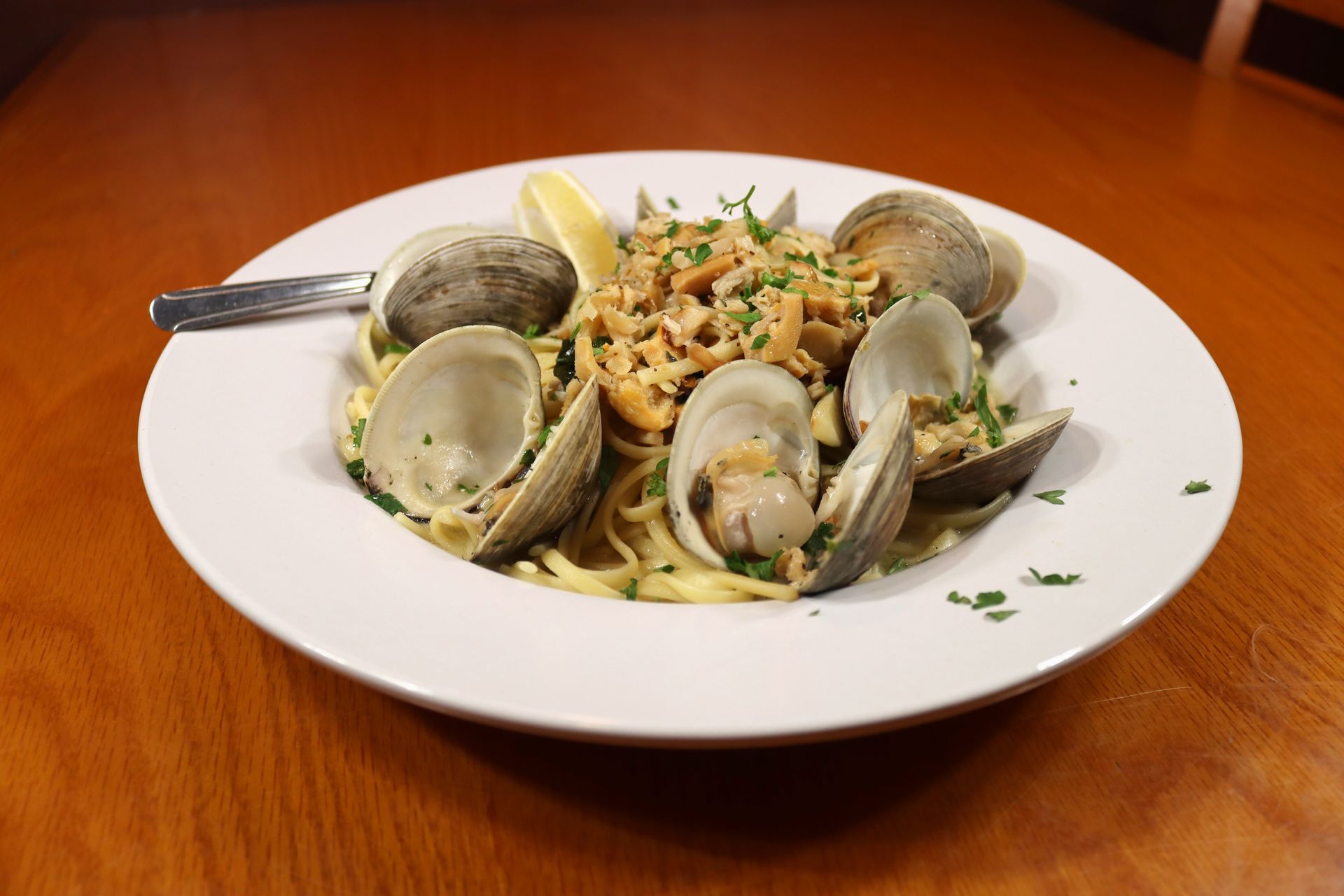 A white plate topped with clams and noodles with a fork on a wooden table.
