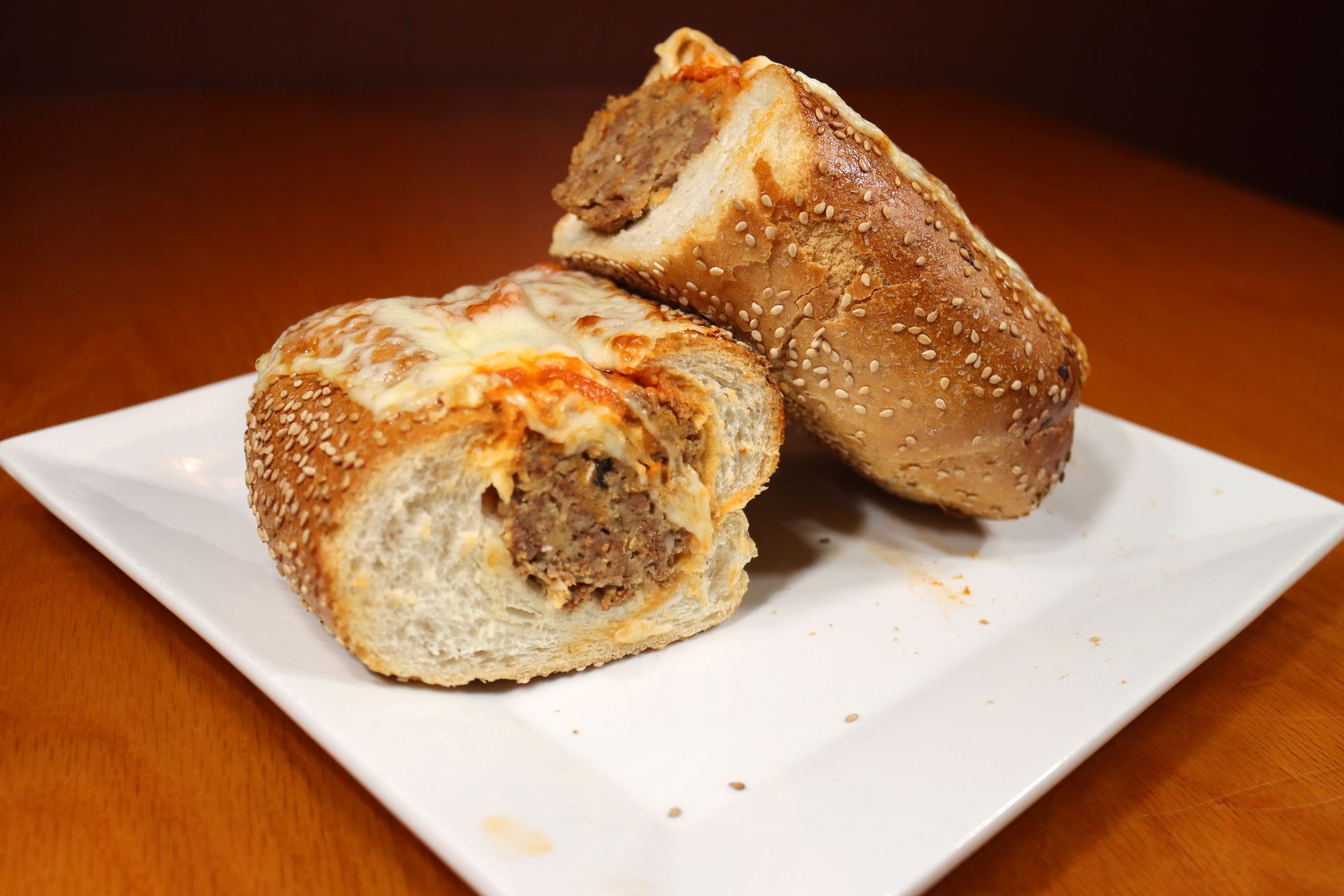 A sausage sandwich is cut in half on a white plate.