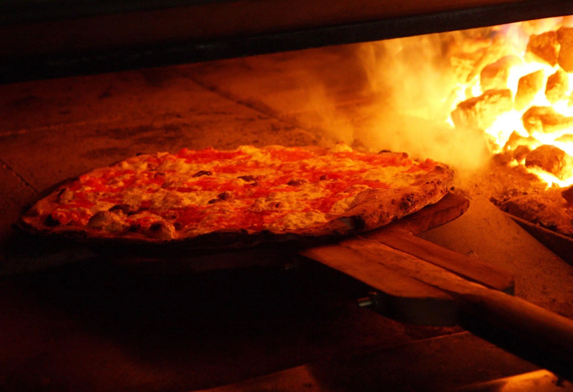 A pizza is being taken out of an oven with flames behind it.