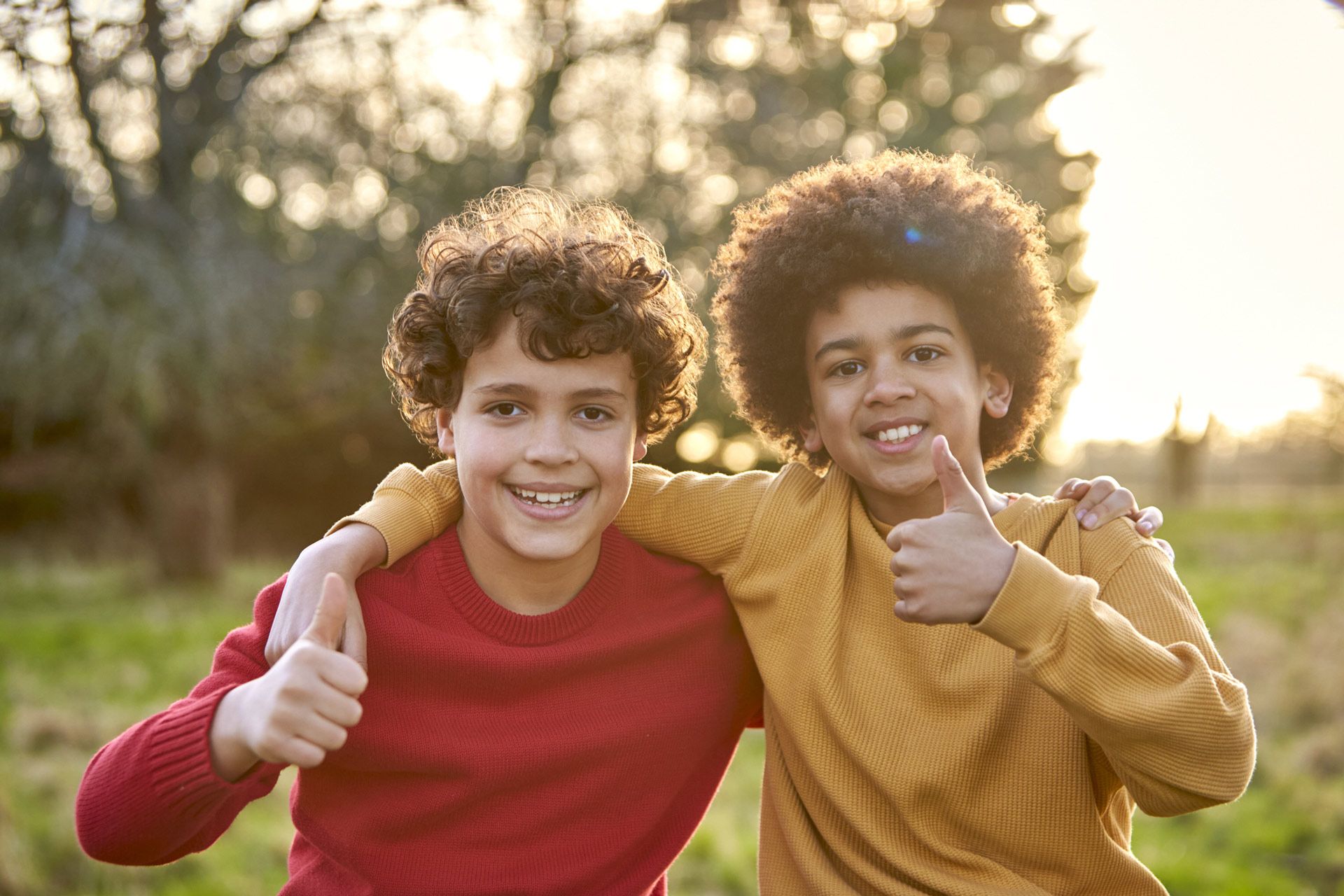 Two young boys are hugging each other and giving a thumbs up.