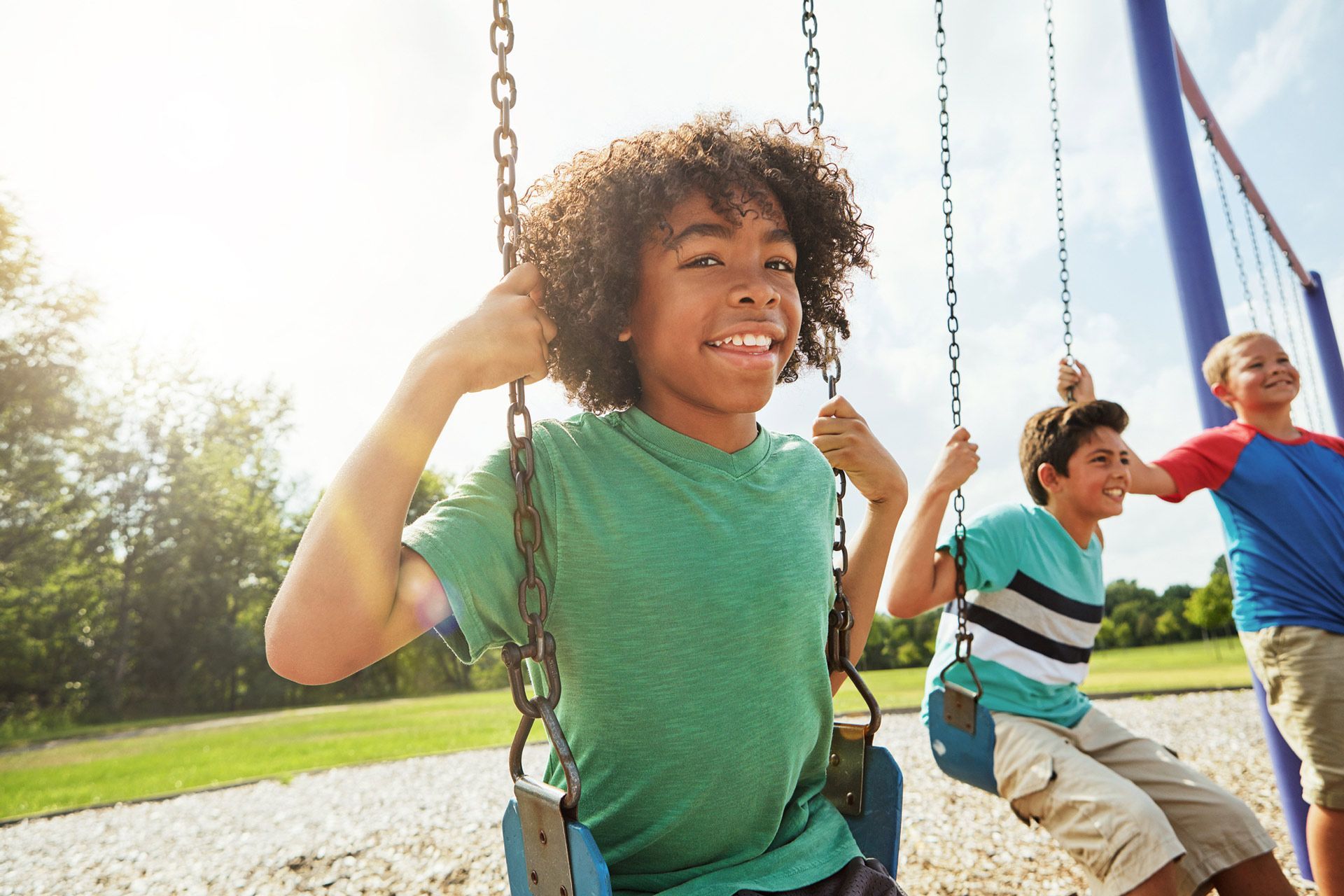 Three young boys are sitting on swings at a playground