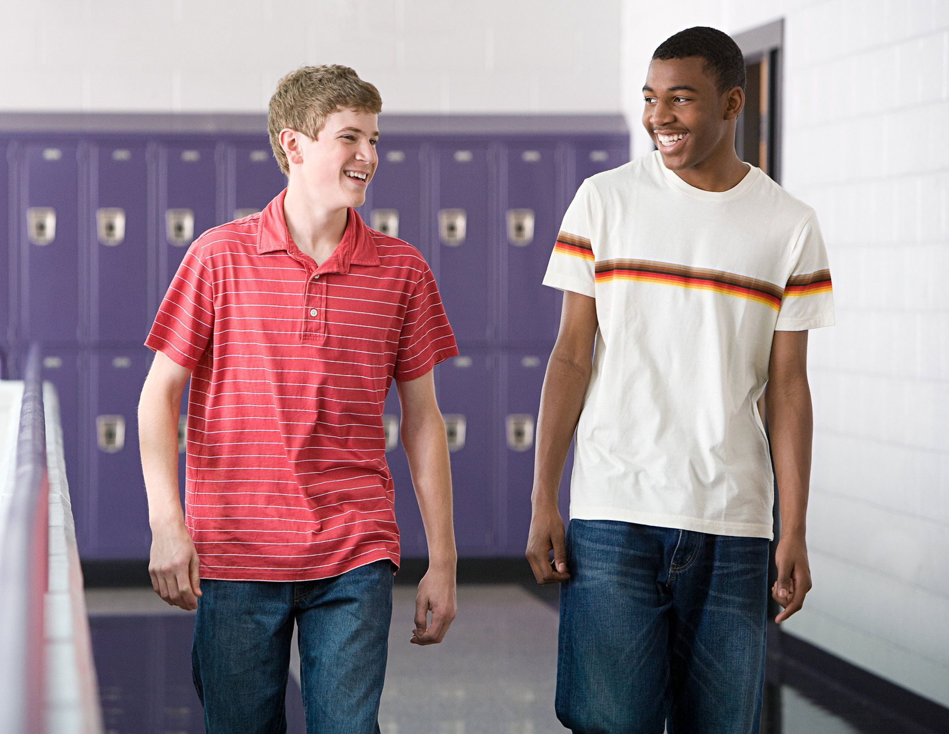 Two boys are walking down a hallway with purple lockers in the background