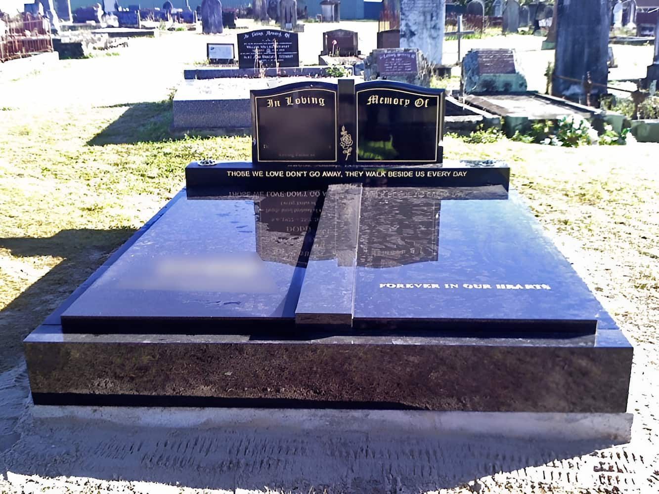 Black granite headstone with two dark uprights and a flat top at a cemetery.