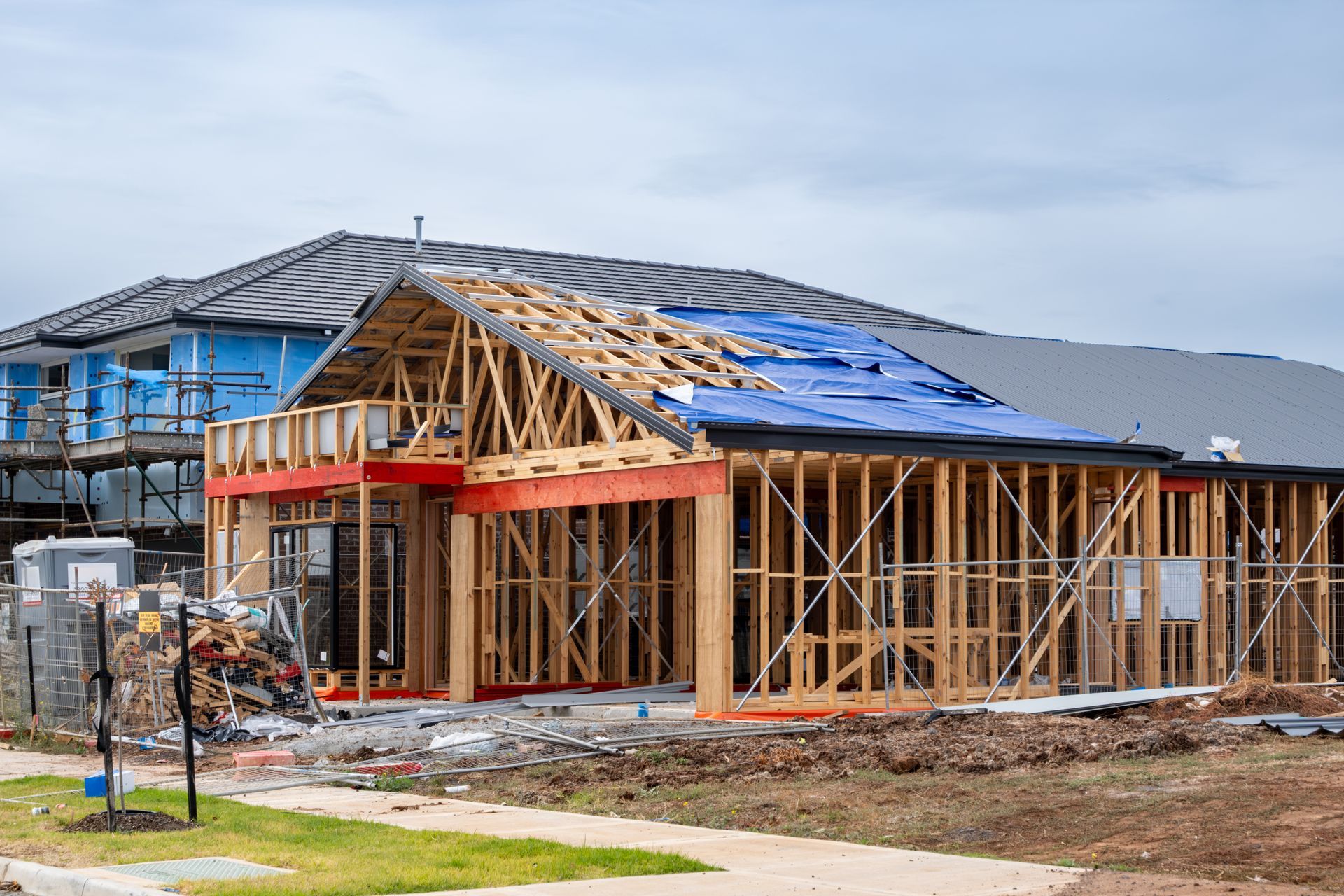 Partially framed house under construction with blue roof tarps and exposed wooden framing