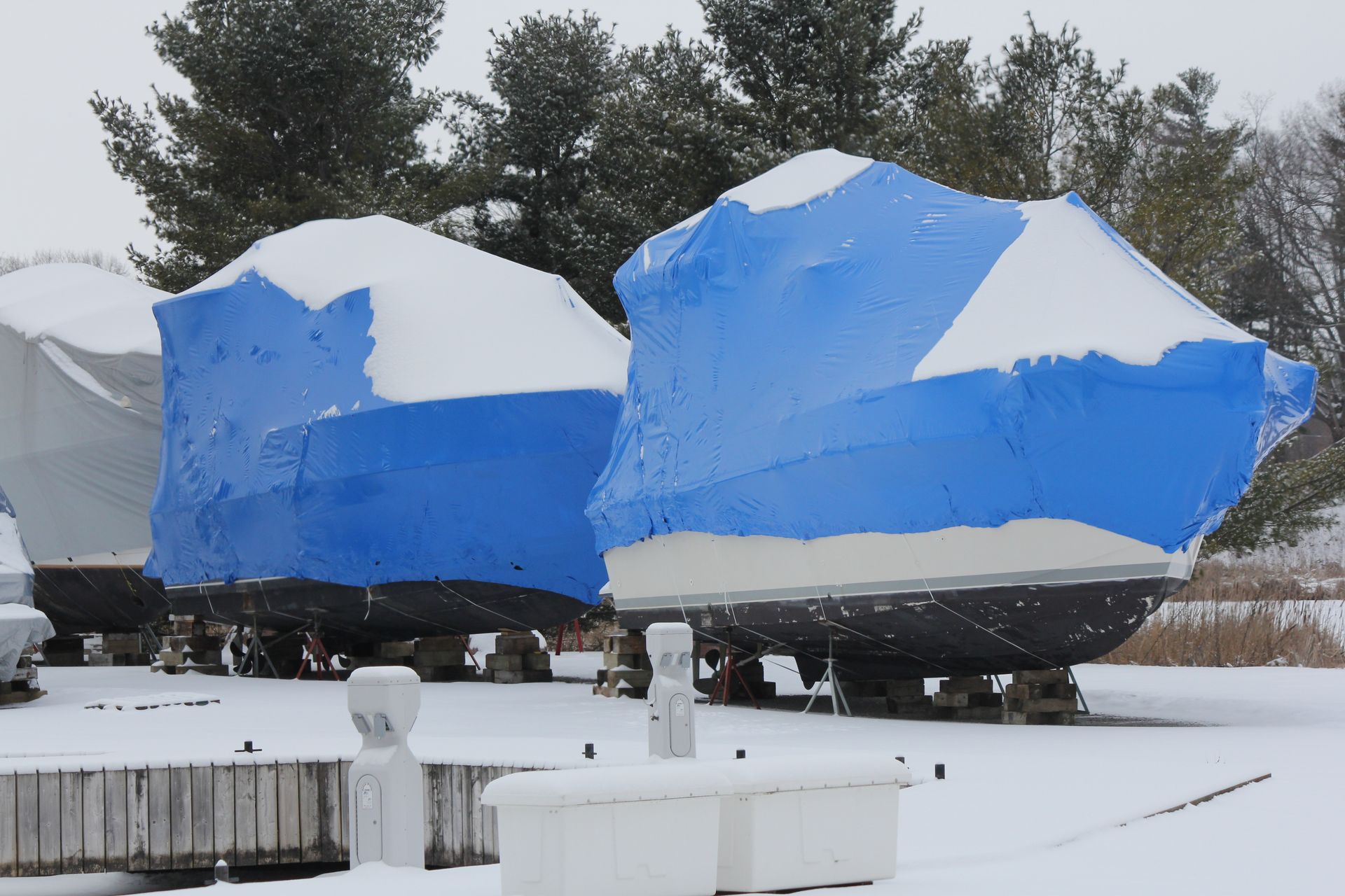 Long flatbed trailer covered with a black tarp, parked on a roadside with trees behind it