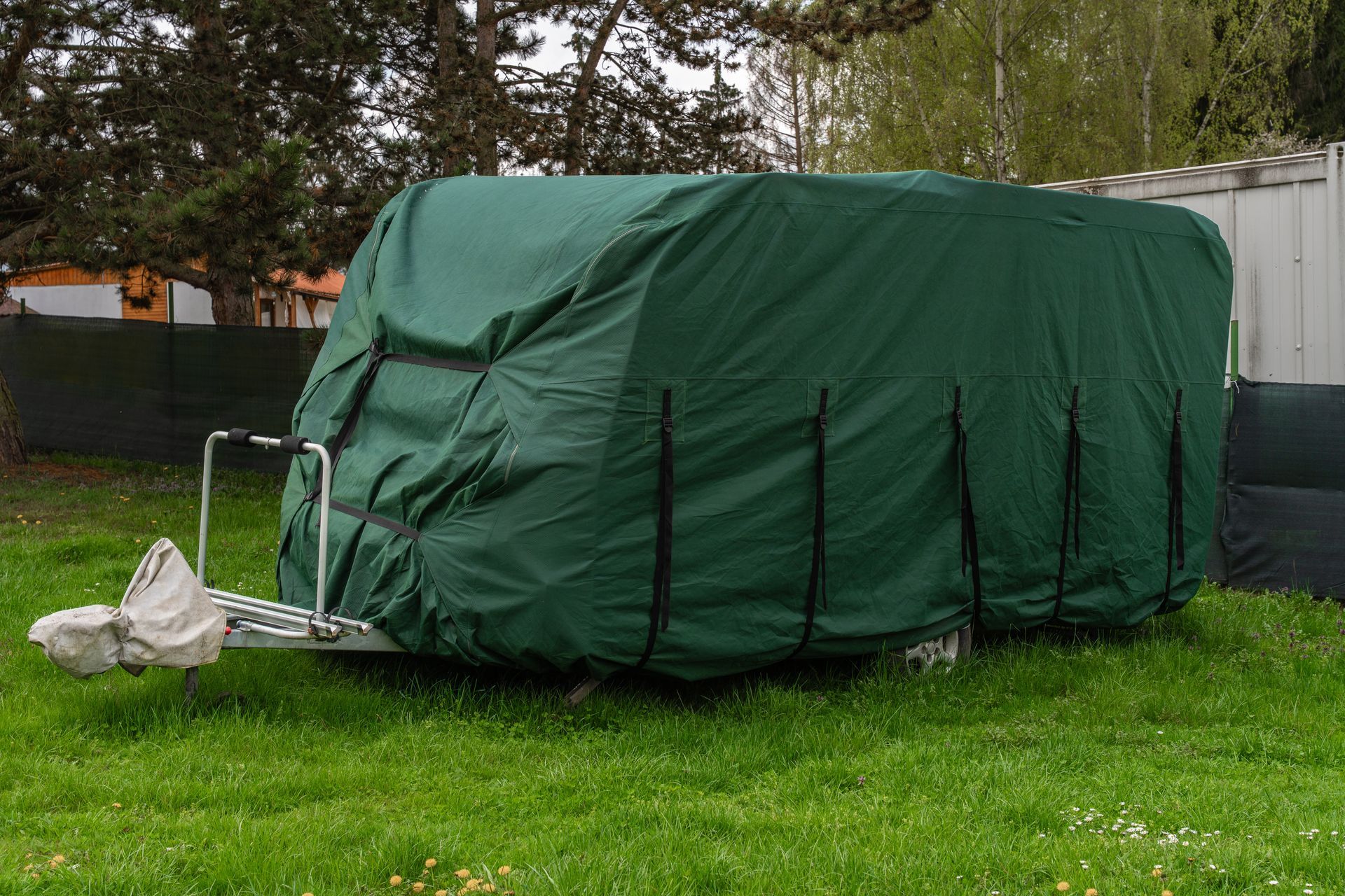 Green tarp-covered trailer or equipment in a grassy yard beside a fence