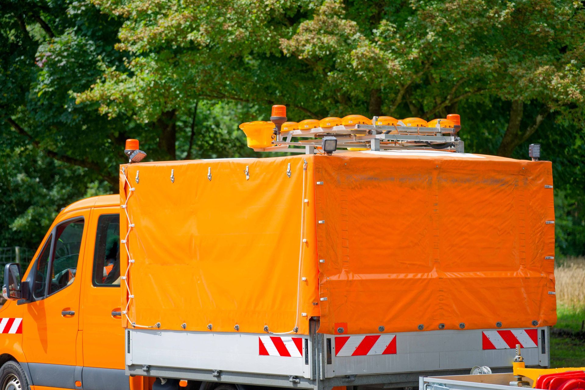 Orange utility truck with roof lights parked outdoors near trees