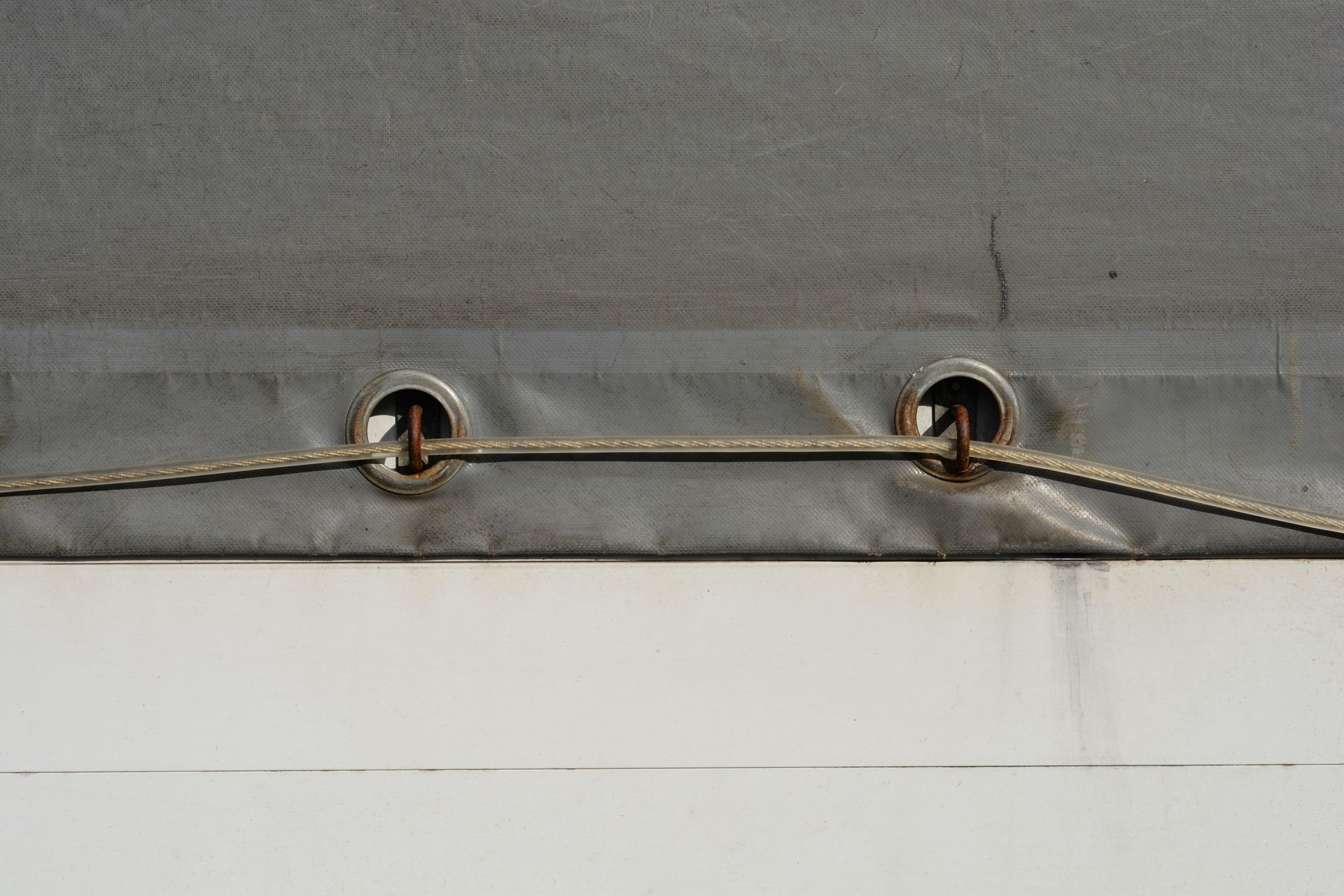 Close-up of a gray fabric cover with two metal grommets threaded by a tan cord Close-up of a gray fabric cover with two metal grommets threaded by a tan cord