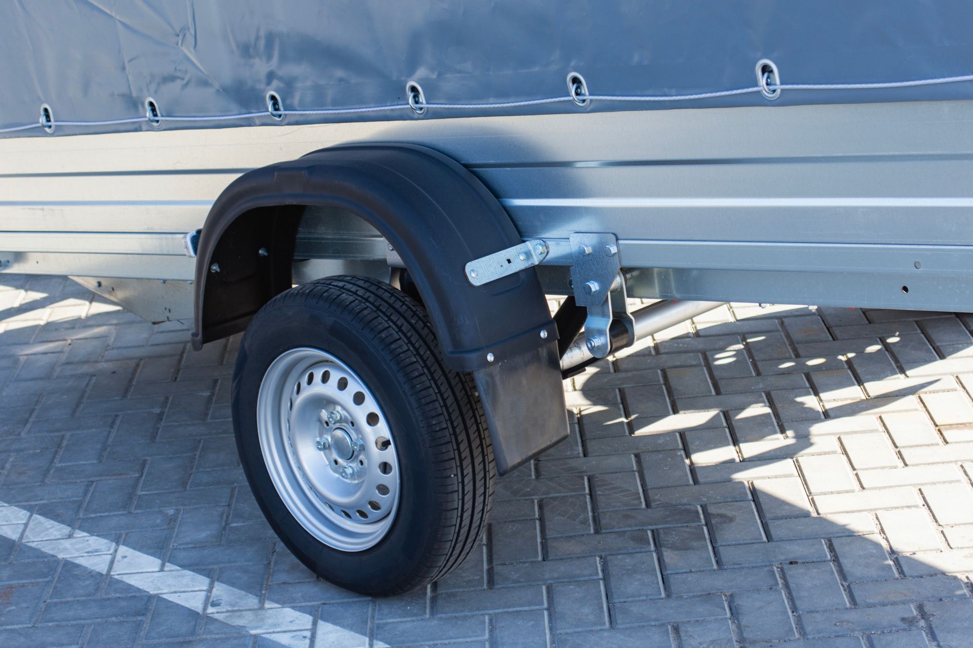 Close-up of a trailer wheel with a black fender beside a silver vehicle on a brick pavement Close-up of a trailer wheel with a black fender beside a silver vehicle on a brick pavement