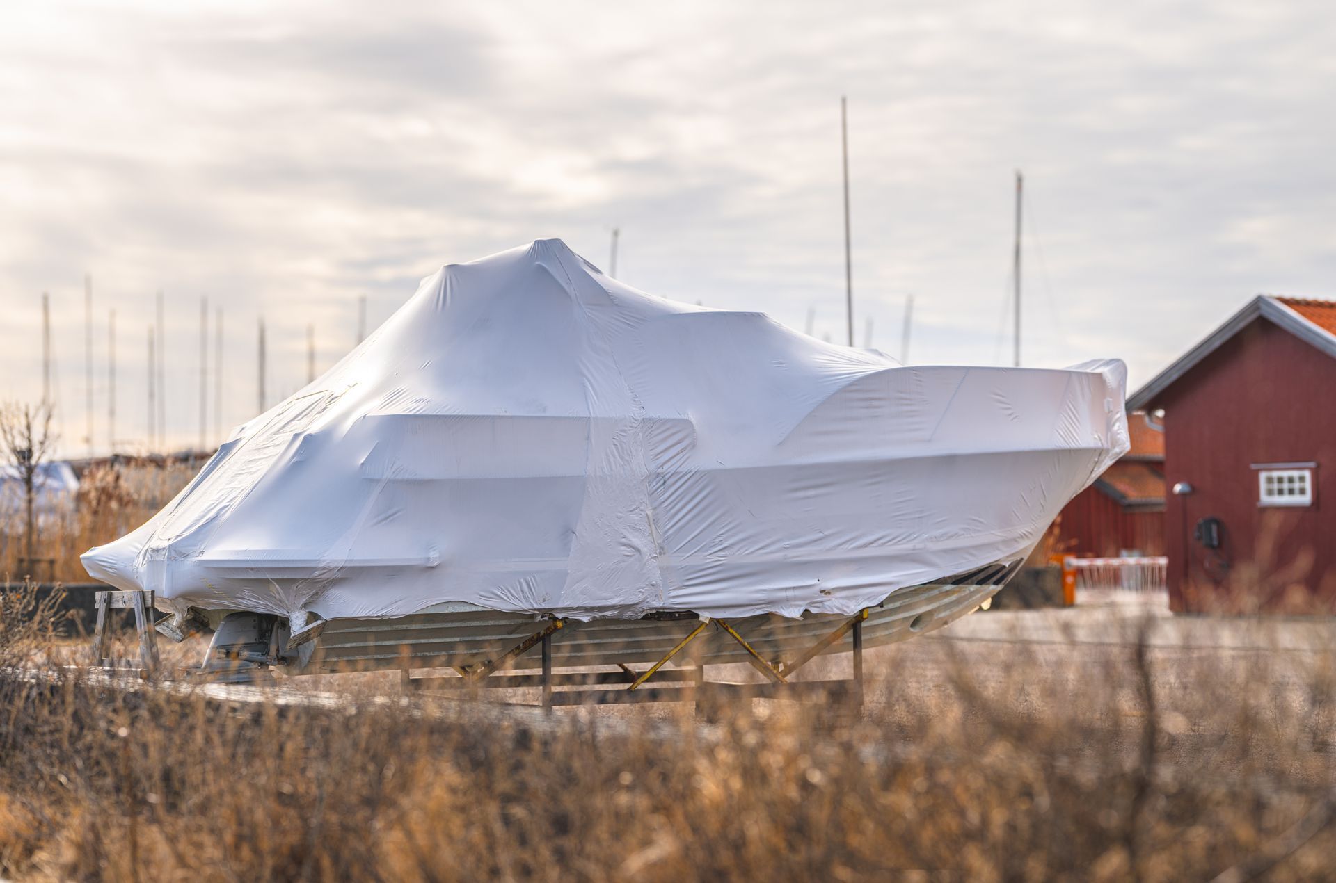 Boat wrapped in white plastic on land near a red barn at sunset