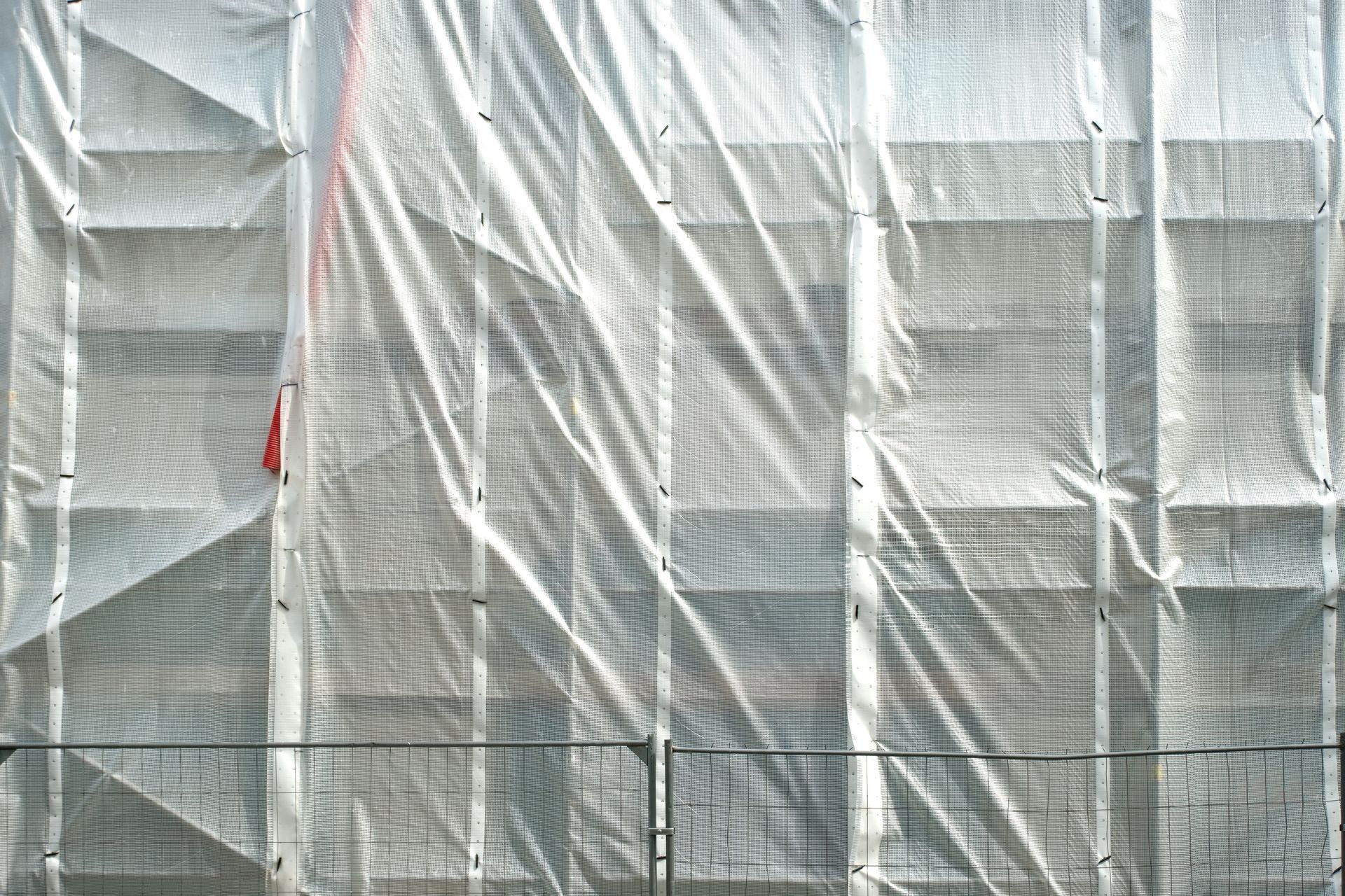 White tarp or sheeting draped over a building scaffold behind a black fence White tarp or sheeting draped over a building scaffold behind a black fence
