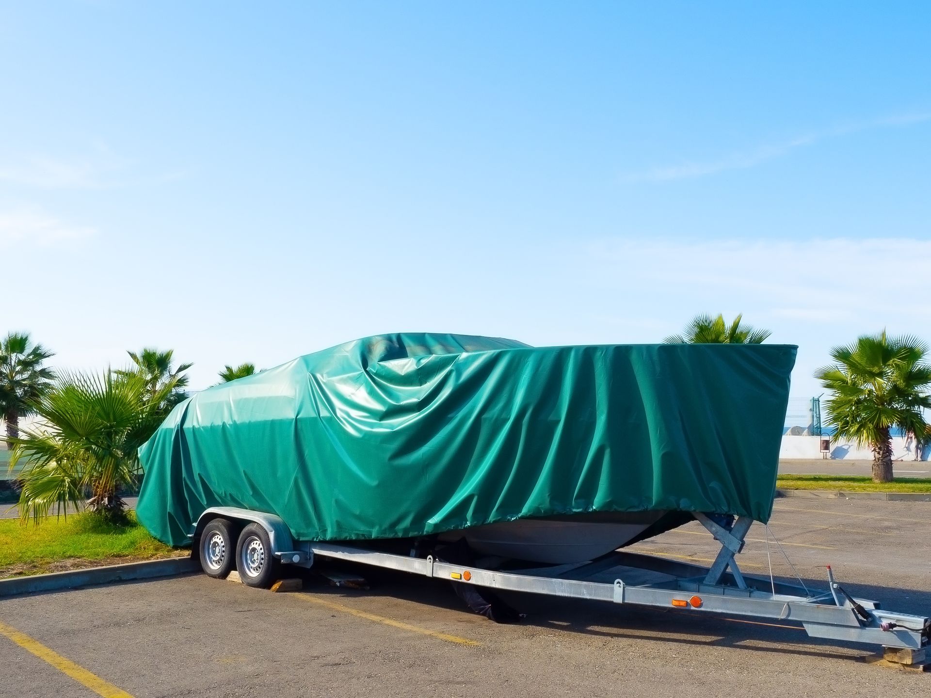 Green tarp-covered boat on a trailer parked outdoors on a roadside.