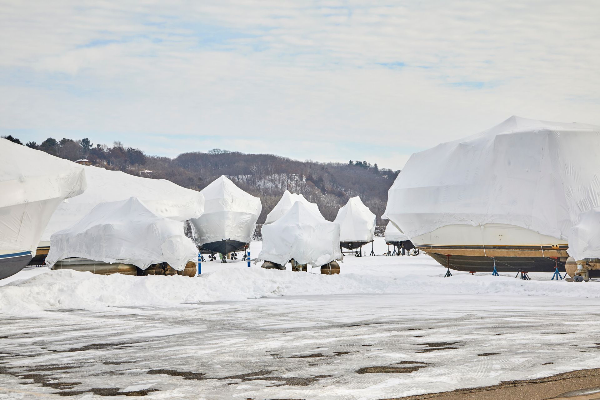 Snow-covered boats stored on a frozen shoreline with mountains in the background