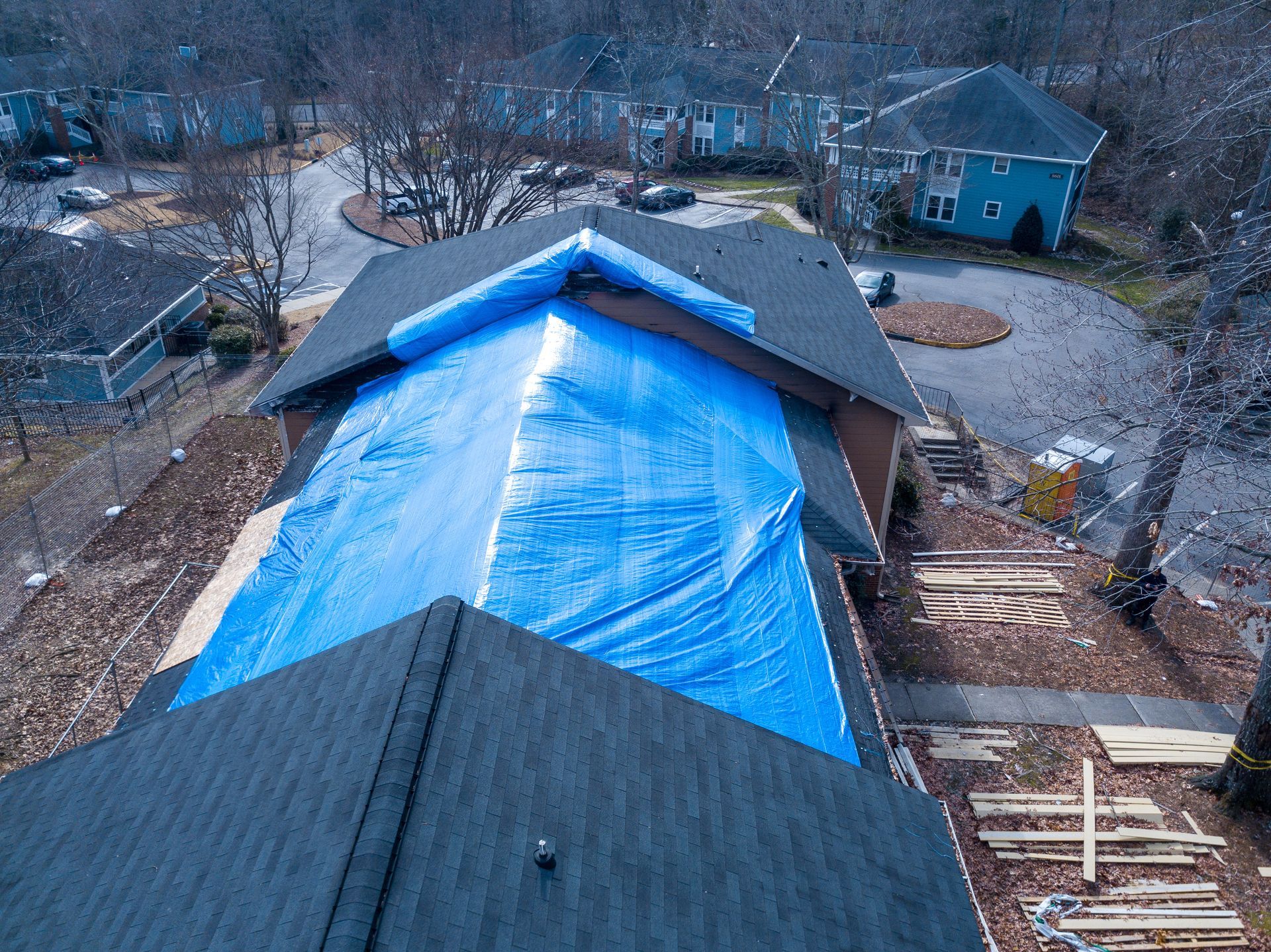 Blue tarp covering a roof under repair on a house in a wooded neighborhood
