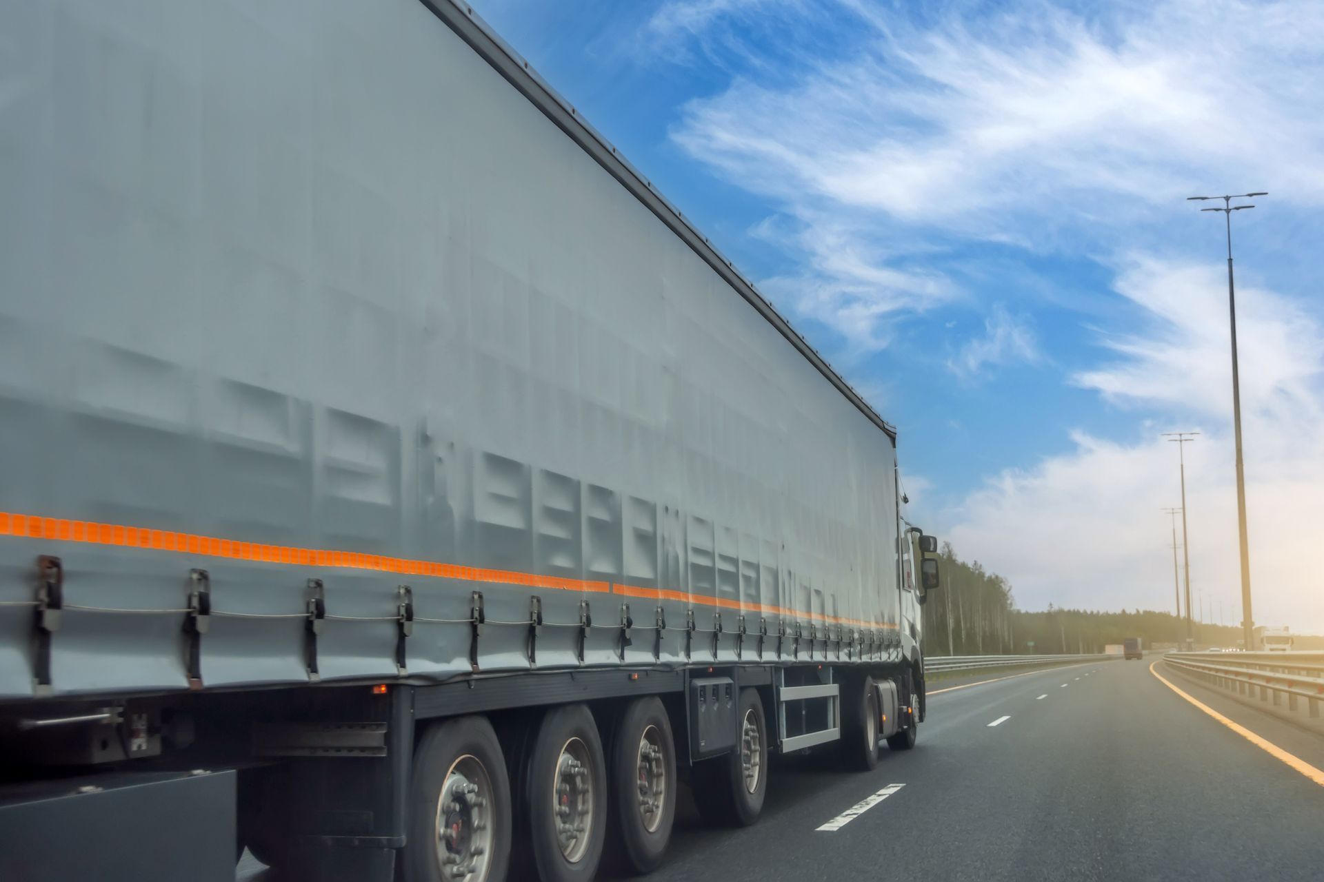 Long semi-trailer truck driving on a highway under a bright blue sky