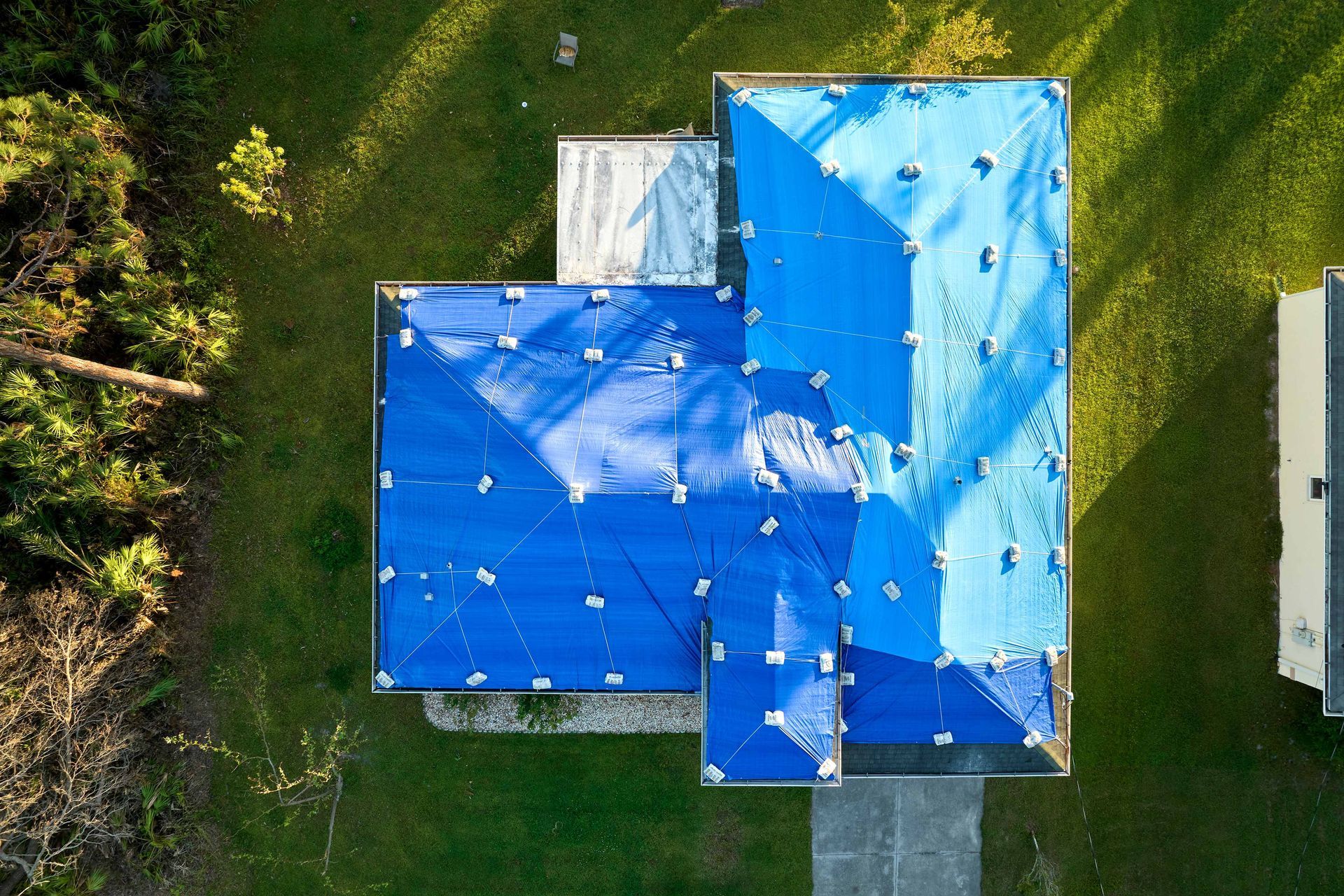 Aerial view of a house with a bright blue roof surrounded by green lawn.