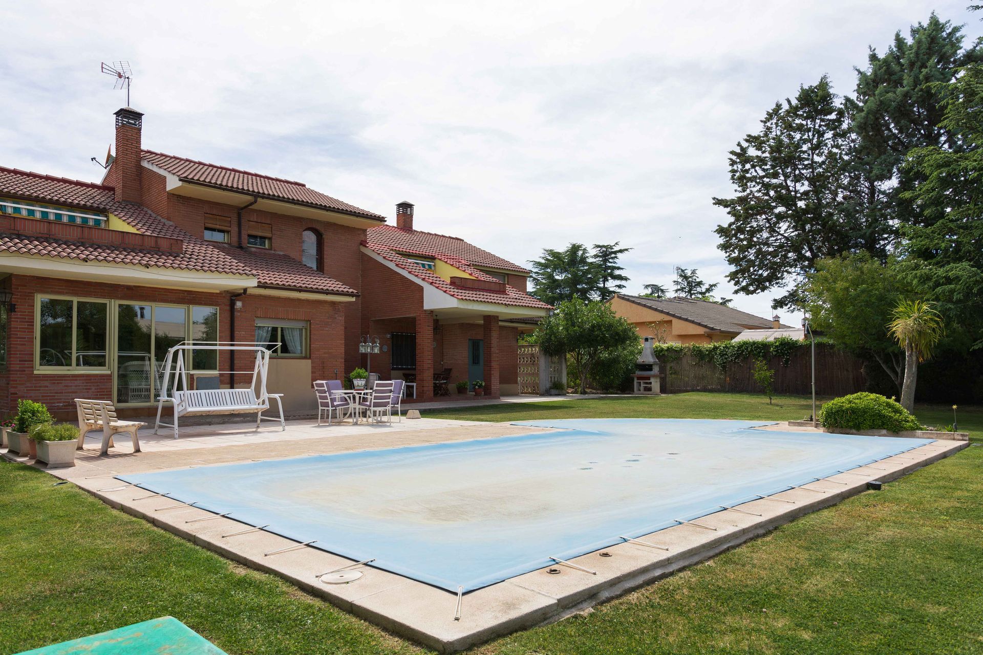 Backyard with a brick house, patio furniture, and a rectangular swimming pool surrounded by lawn.