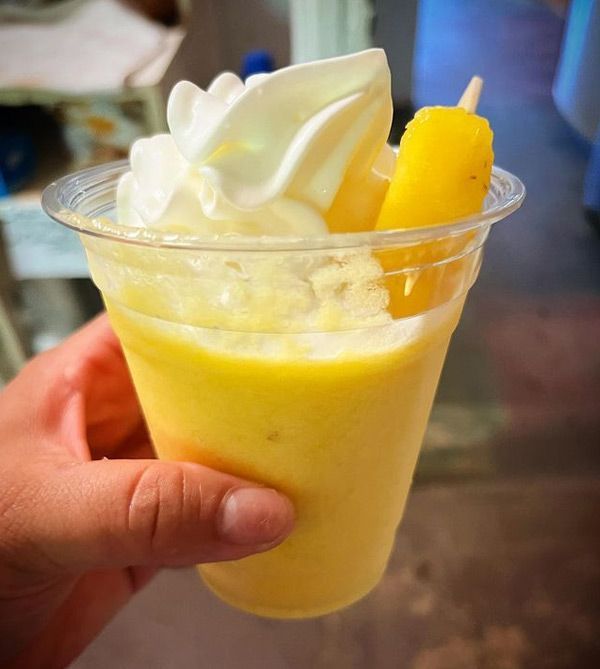 A person is holding a cup of ice cream with whipped cream and a pineapple slice