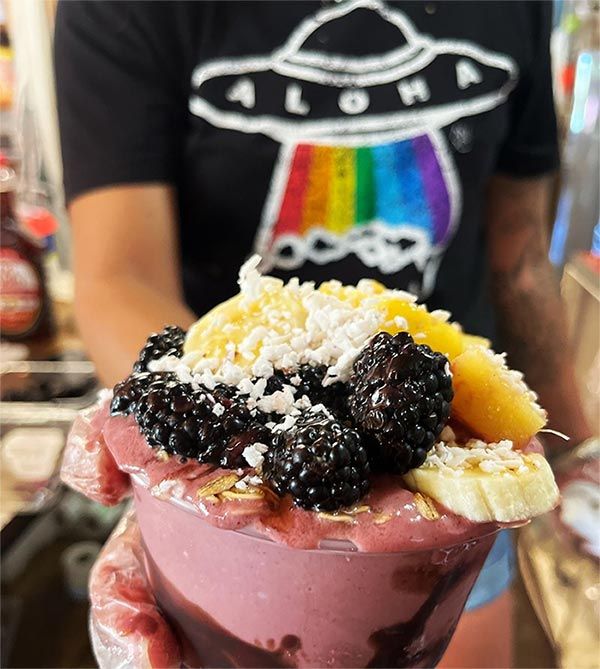 A person wearing an aloha shirt is holding a bowl of fruit