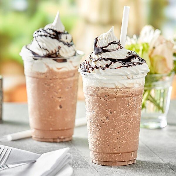 Two cups of chocolate milkshakes with whipped cream and chocolate sauce on a table.