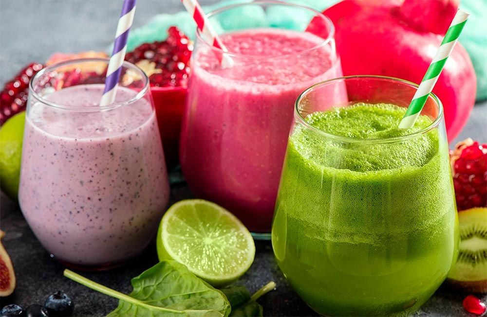 Three different smoothies in glasses with straws on a table.