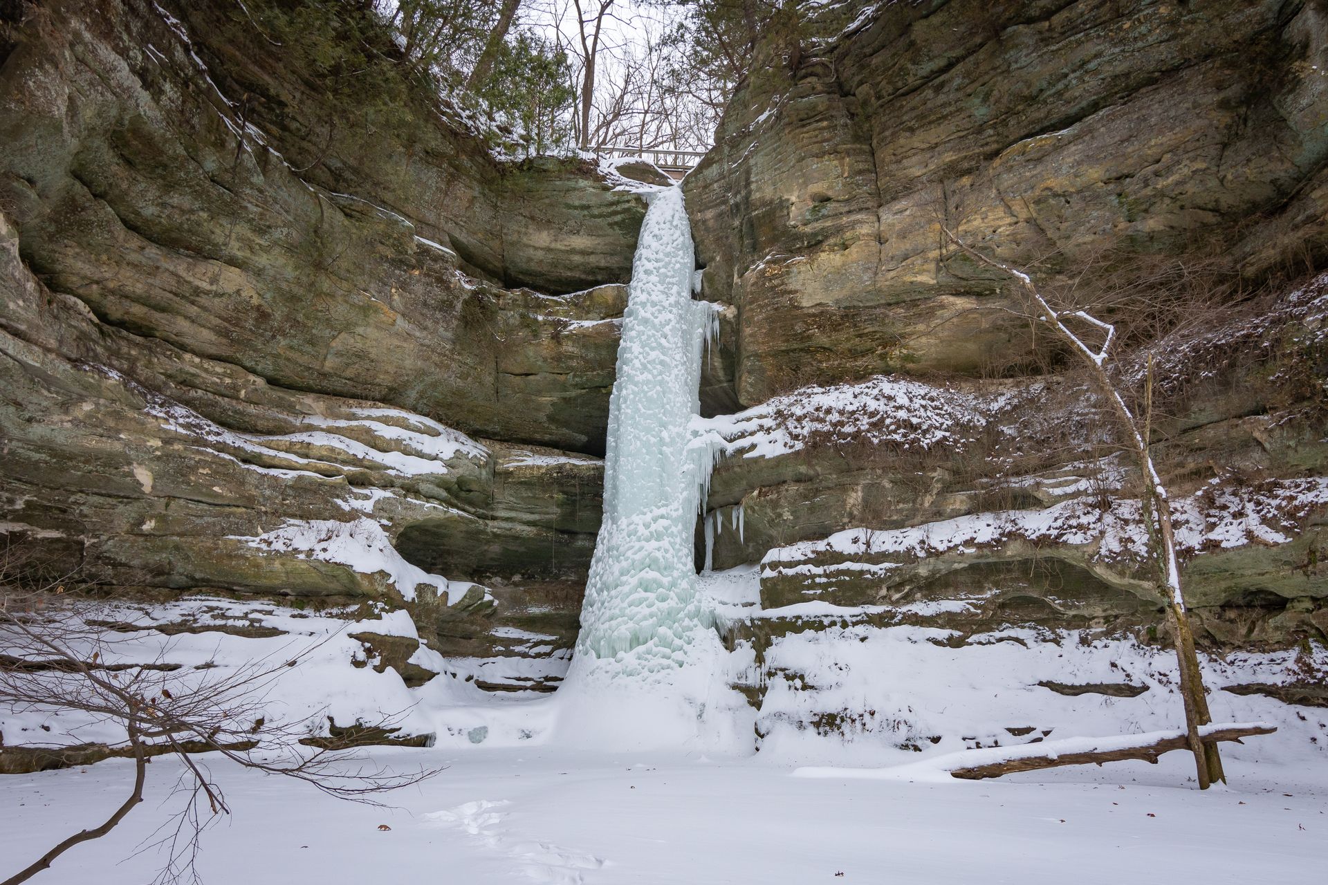 Frozen waterfall in a rocky cliff with snow-covered ground and bare trees