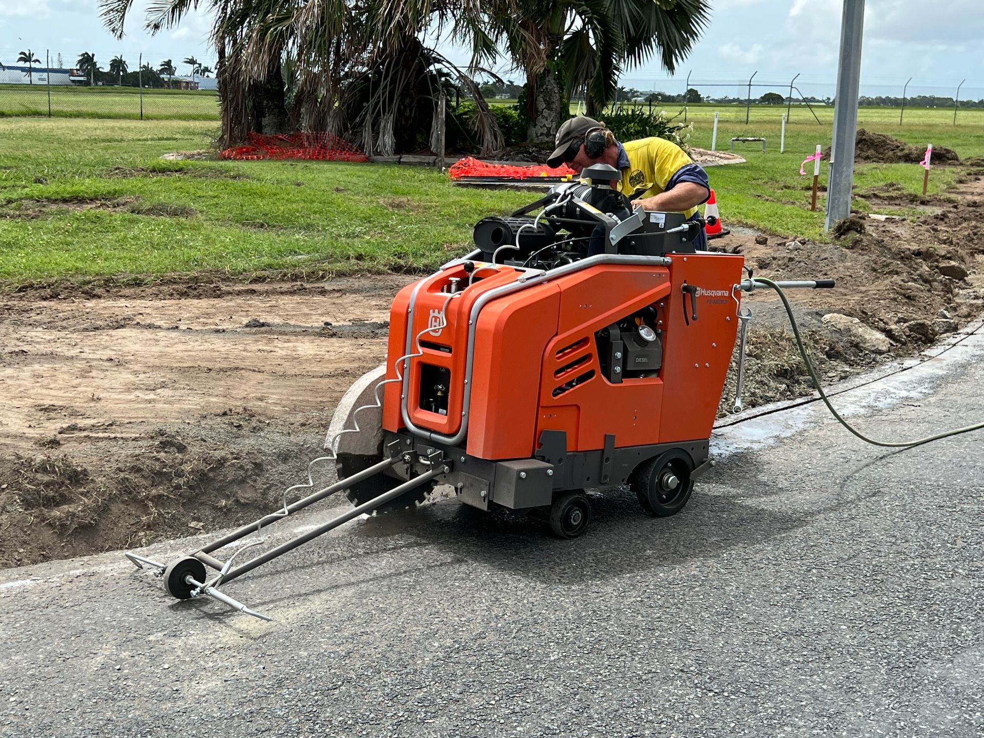 Worker operating an orange road marking machine on a roadside near a grassy field. — Ablecut Concrete Cutting & Coring In East Mackay, QLD