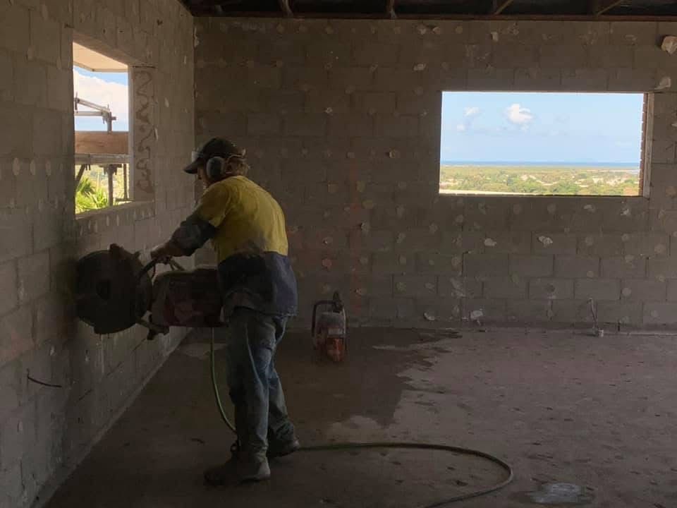 Worker in yellow shirt using a power tool to cut a wall inside an unfinished brick room. — Ablecut Concrete Cutting & Coring In East Mackay, QLD