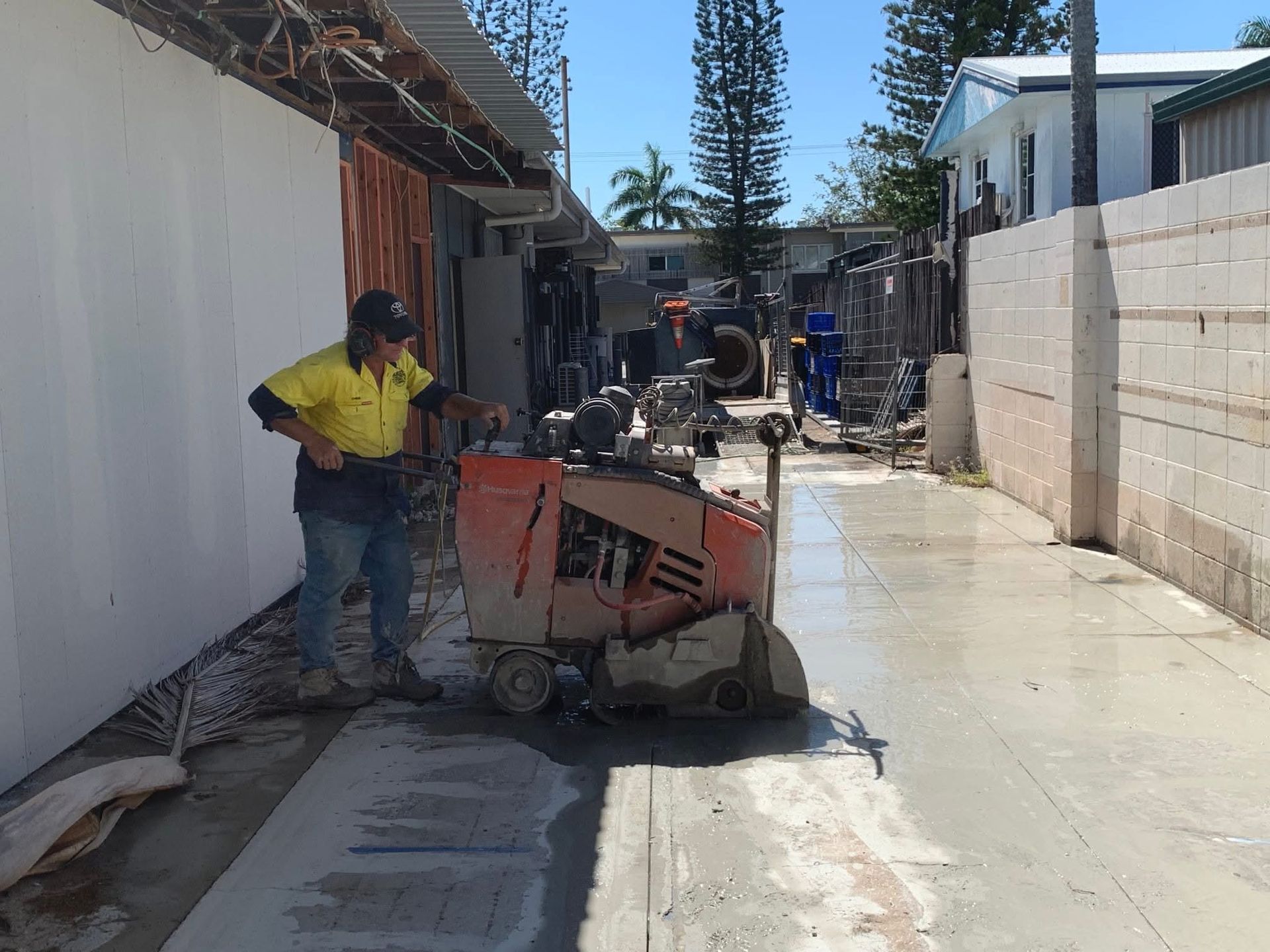 Hands Using a Blue Angle Grinder to Cut a Gray Concrete Wall — Ablecut Concrete Cutting & Coring In East Mackay, QLD