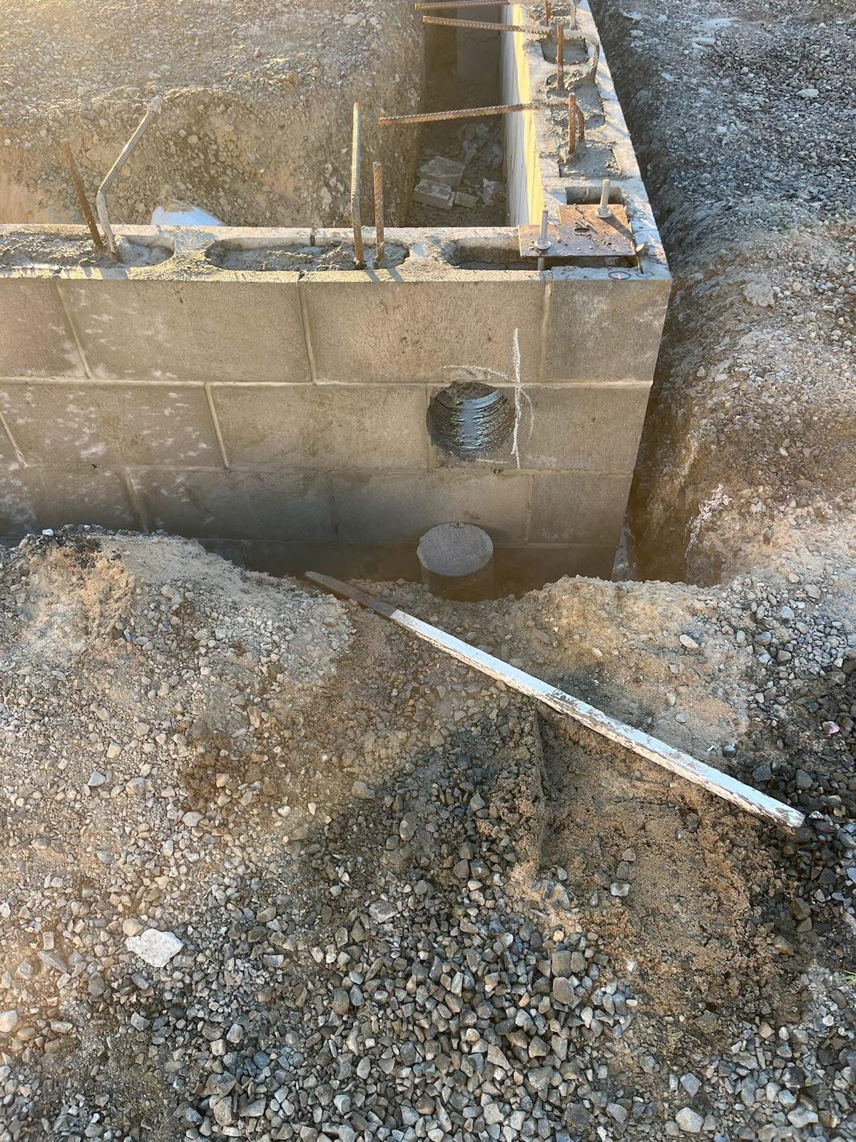 Partially built cinder block wall with gravel, soil trench, and a white pipe in a construction site — Ablecut Concrete Cutting & Coring In East Mackay, QLD