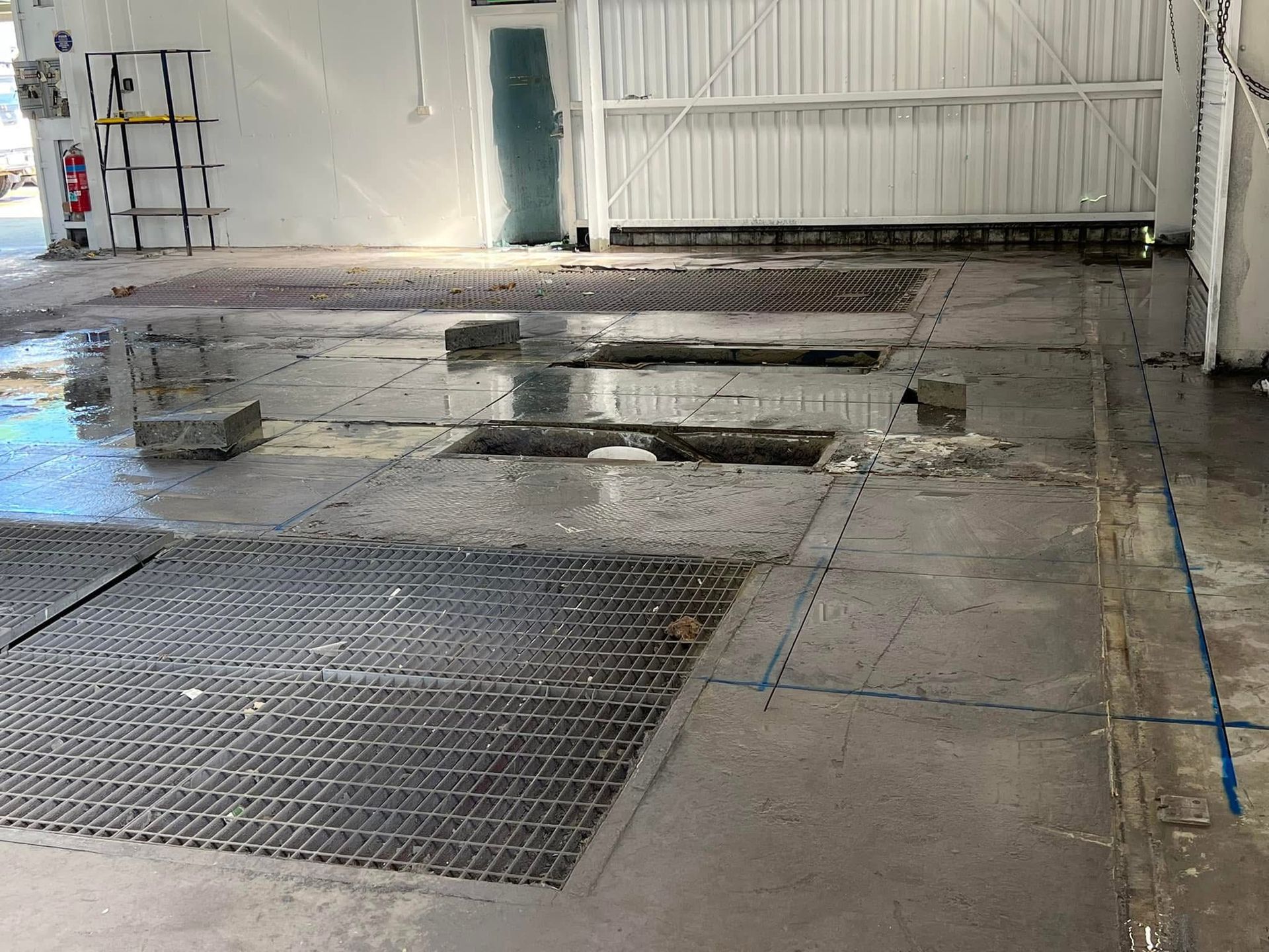 Wet industrial floor with puddles, metal grates, and a white wall in a warehouse-like room — Ablecut Concrete Cutting & Coring In East Mackay, QLD