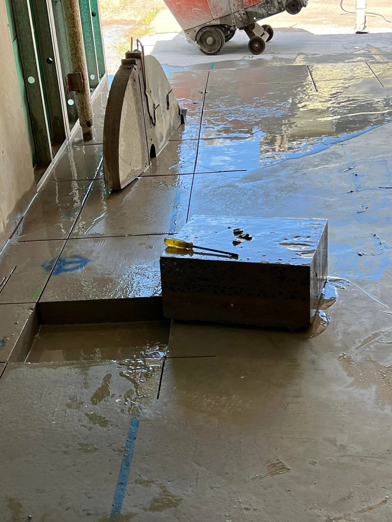 Mud-covered floor with a wet saw and a small black block in a worksite or garage. — Ablecut Concrete Cutting & Coring In East Mackay, QLD