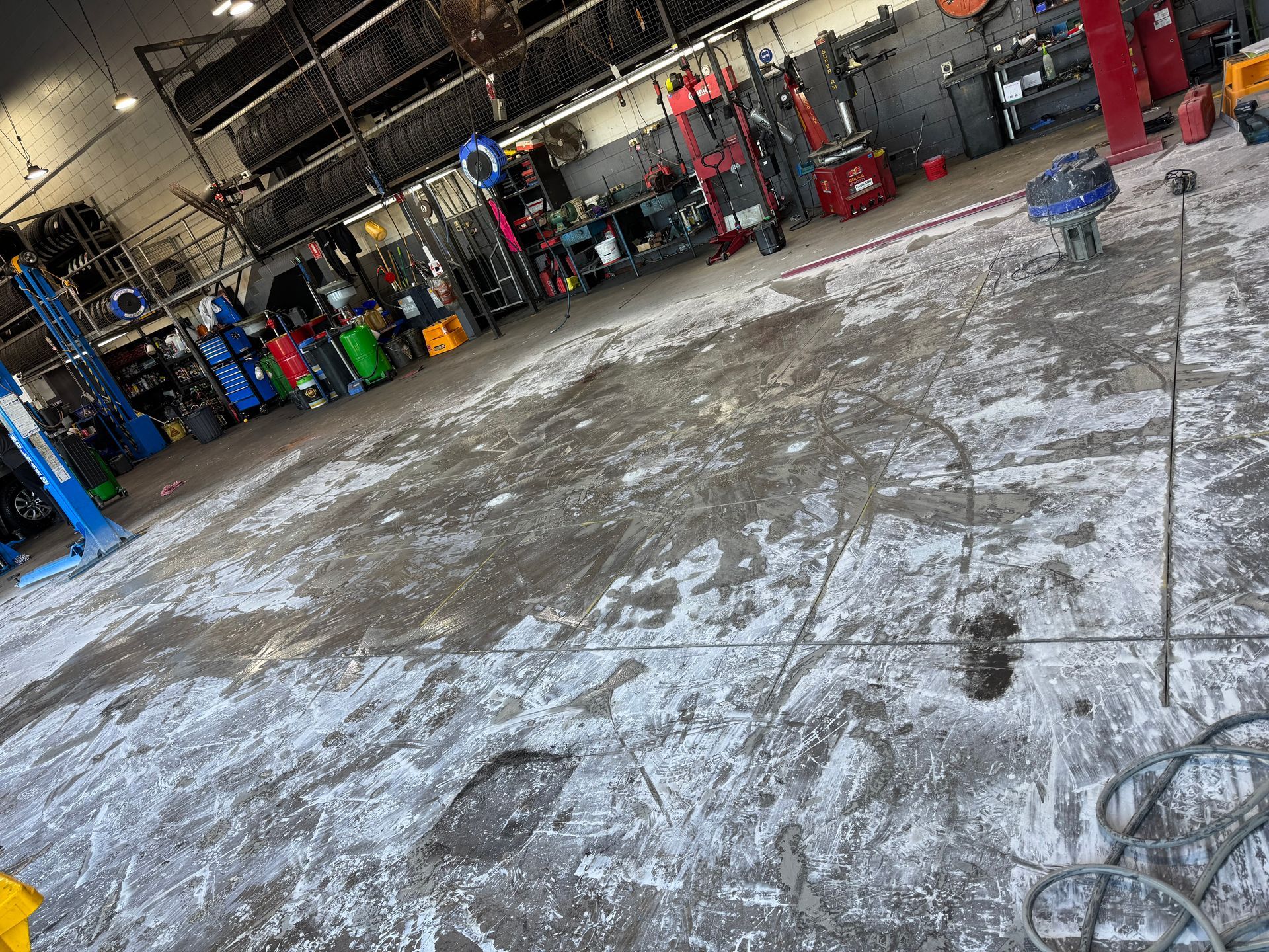 Large auto repair shop with a wet concrete floor, tool racks, and car lifts in the background — Ablecut Concrete Cutting & Coring In East Mackay, QLD