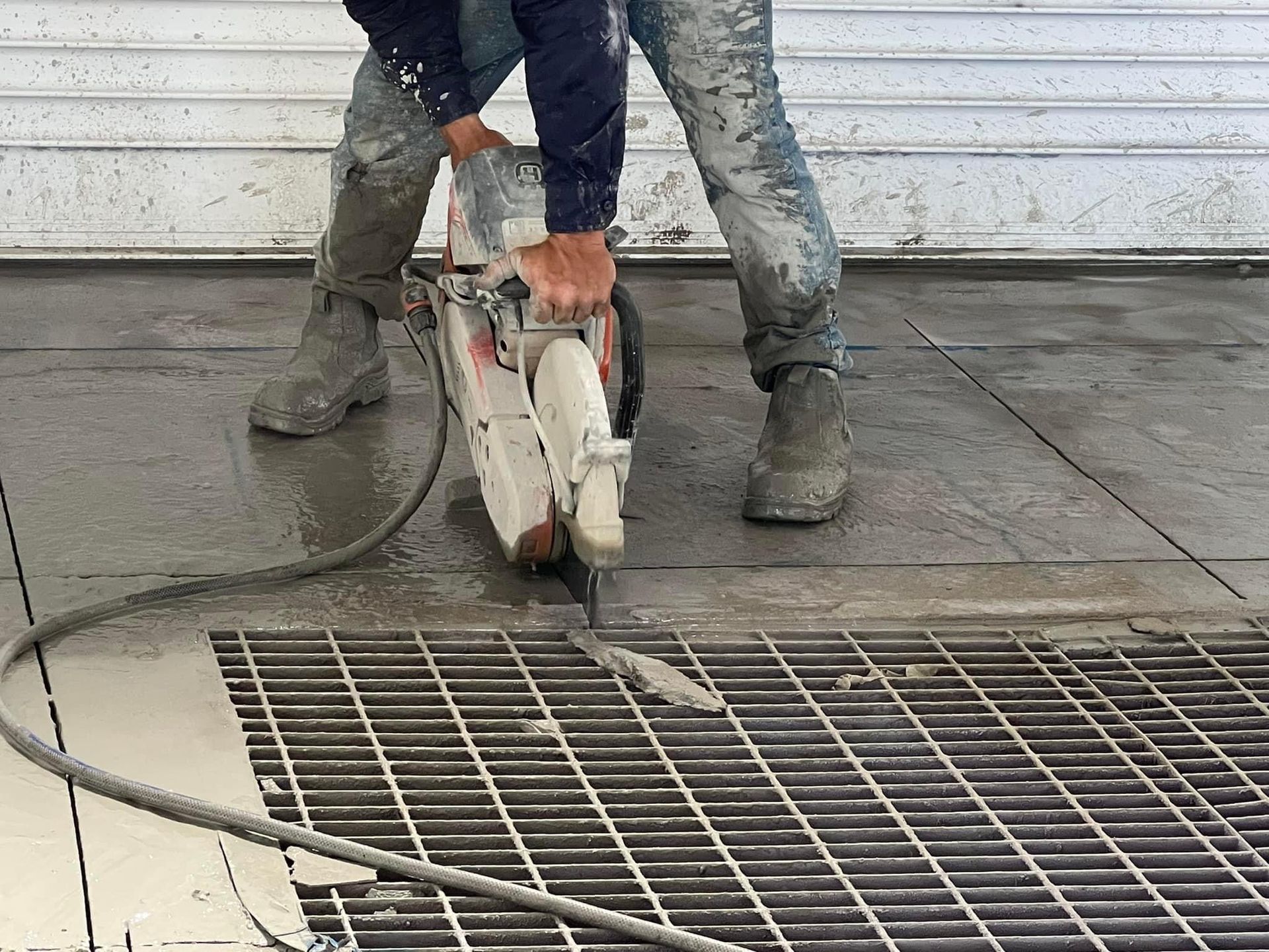 Worker cutting concrete slab with a handheld saw beside a metal floor grate. — Ablecut Concrete Cutting & Coring In East Mackay, QLD