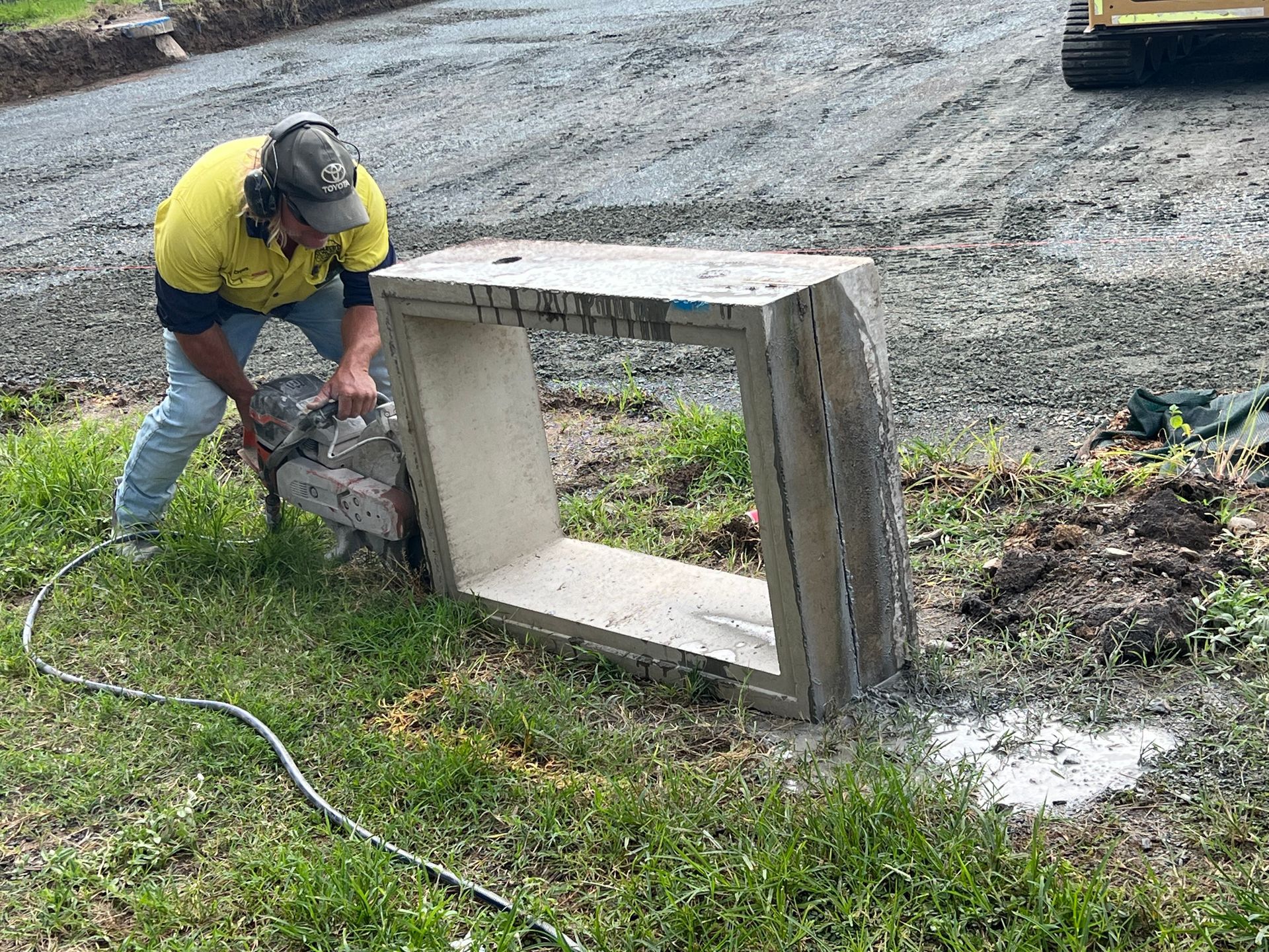 Worker in a yellow shirt stacking concrete blocks beside a roadside drain. — Ablecut Concrete Cutting & Coring In East Mackay, QLD
